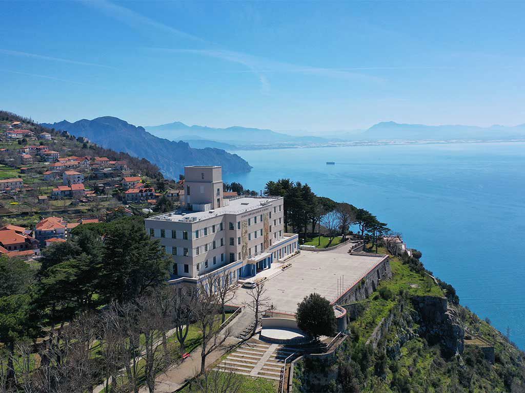 Ein modernes Gebäude am Meer, umgeben von Hügeln und atemberaubender Aussicht auf das Wasser und die Berge.