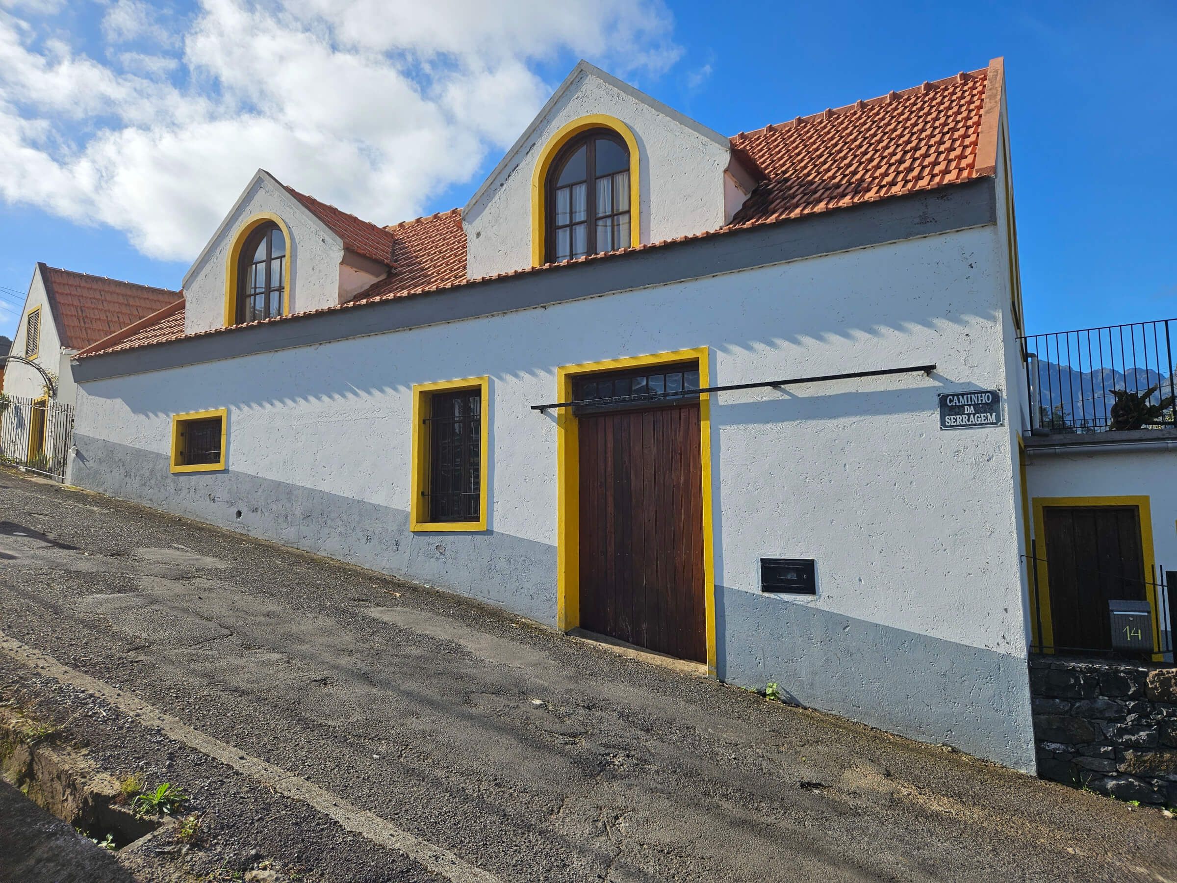 Ein weißes Gebäude mit gelben Akzenten und roten Dächern, steht an einer steilen Straße unter blauem Himmel.