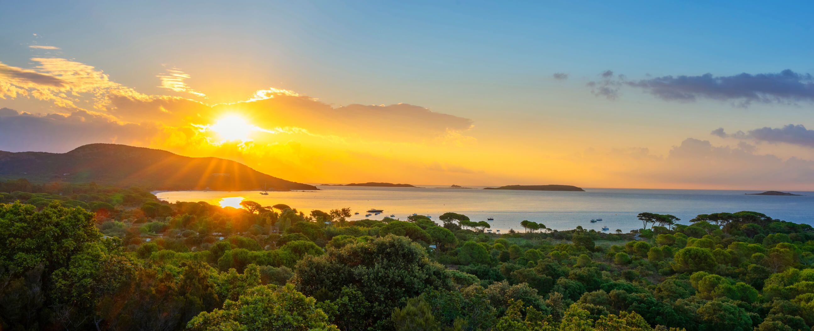 Ein malerischer Sonnenuntergang über einem ruhigen Meer, umgeben von grünen Hügeln und sanften Wellen.