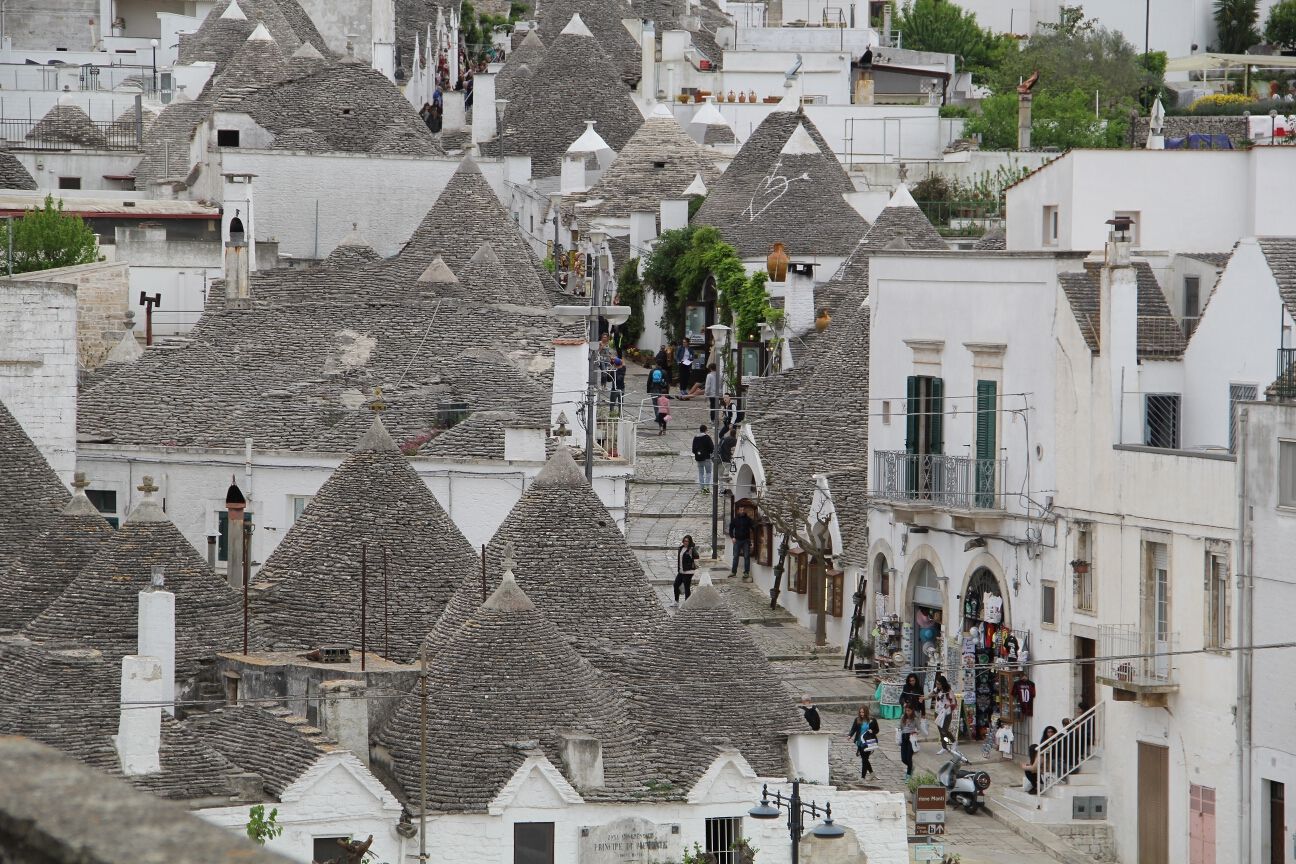 Eine malerische Straße mit Trulli-Häusern in einem charmanten Dorf, viele Besucher schlendern umher.