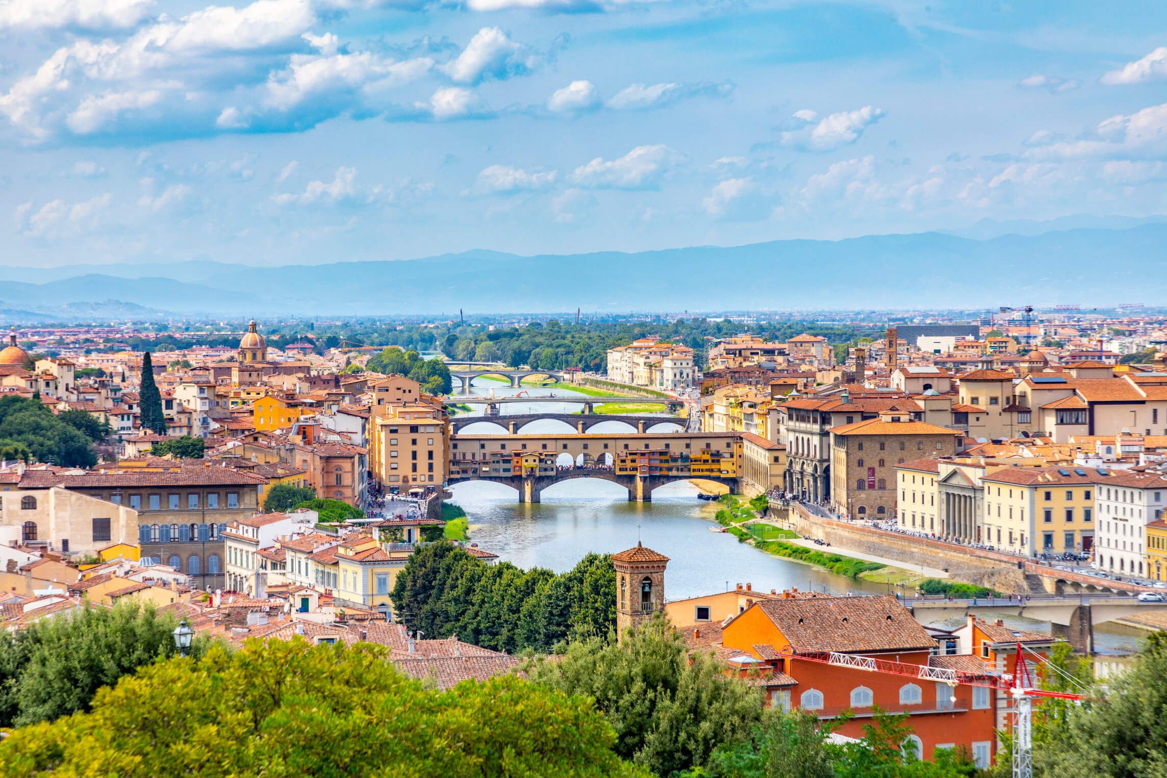 Eine malerische Aussicht auf Florenz mit dem Ponte Vecchio und der Umgebung unter blauem Himmel.