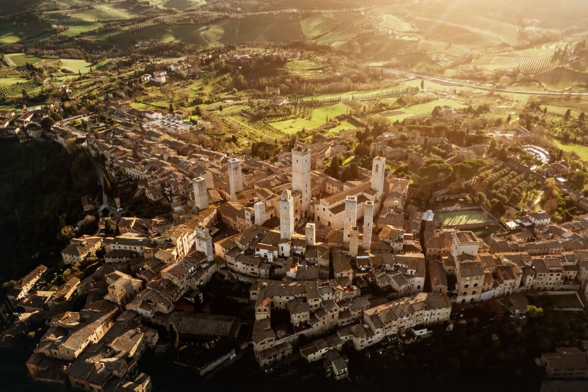 Eine malerische, historische Stadt mit Türmen, umgeben von grünen Hügeln und Landschaften im warmen Licht.