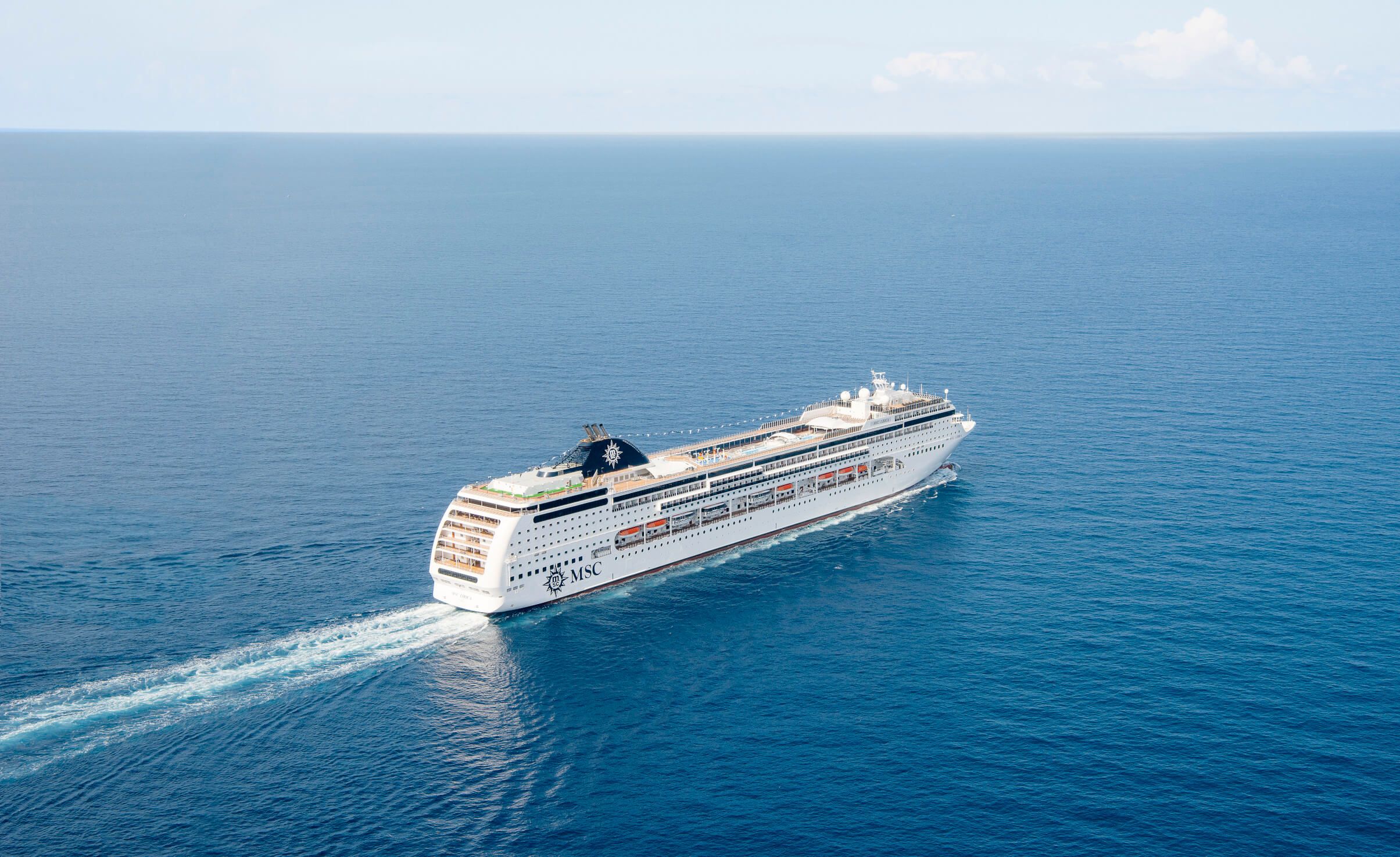 Ein großes Kreuzfahrtschiff fährt über das tiefblaue Wasser des Ozeans unter einem klaren Himmel.