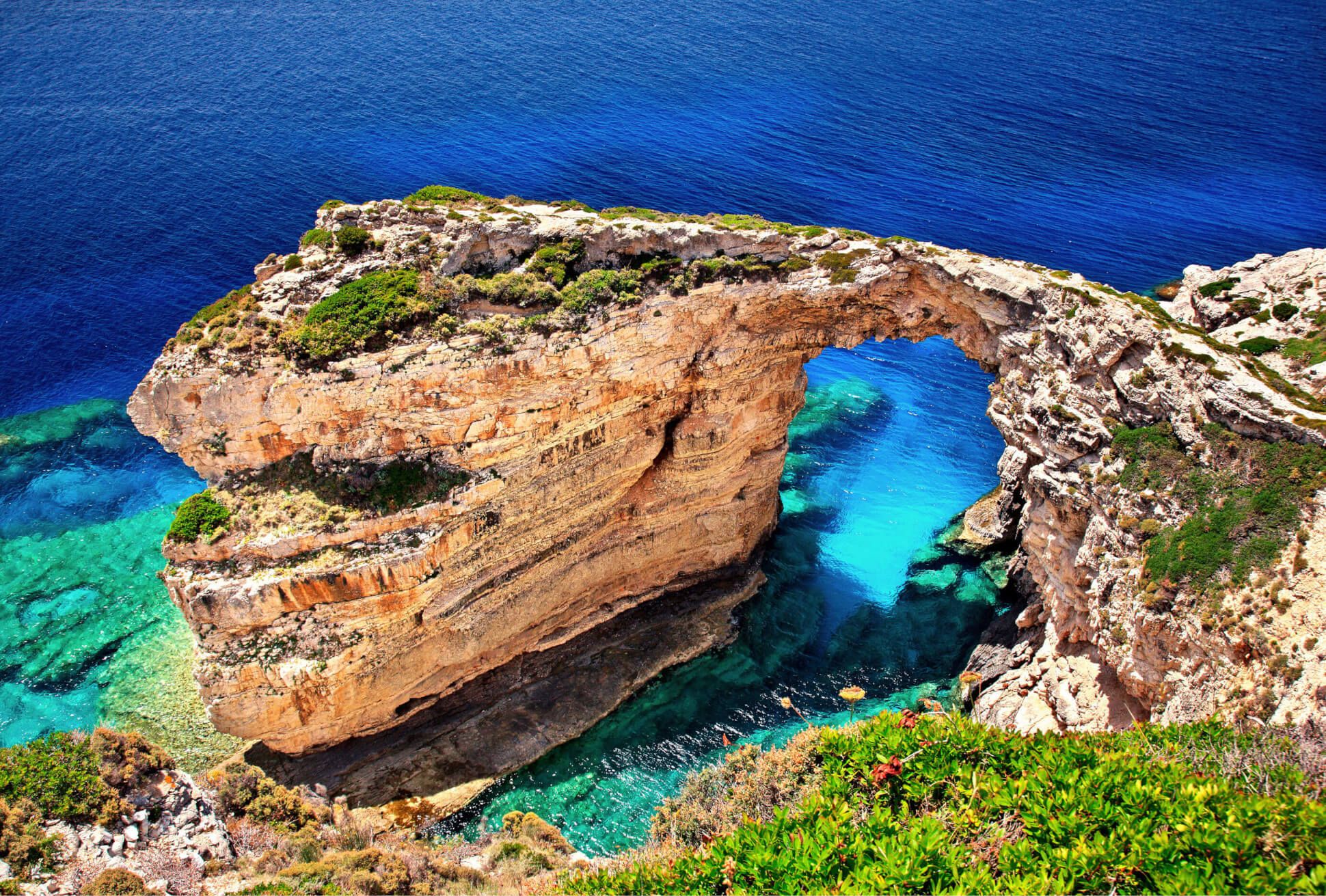 Eine beeindruckende Felsformation mit einem natürlichen Bogen, umgeben von türkis-blauem Wasser und grünem Gelände.