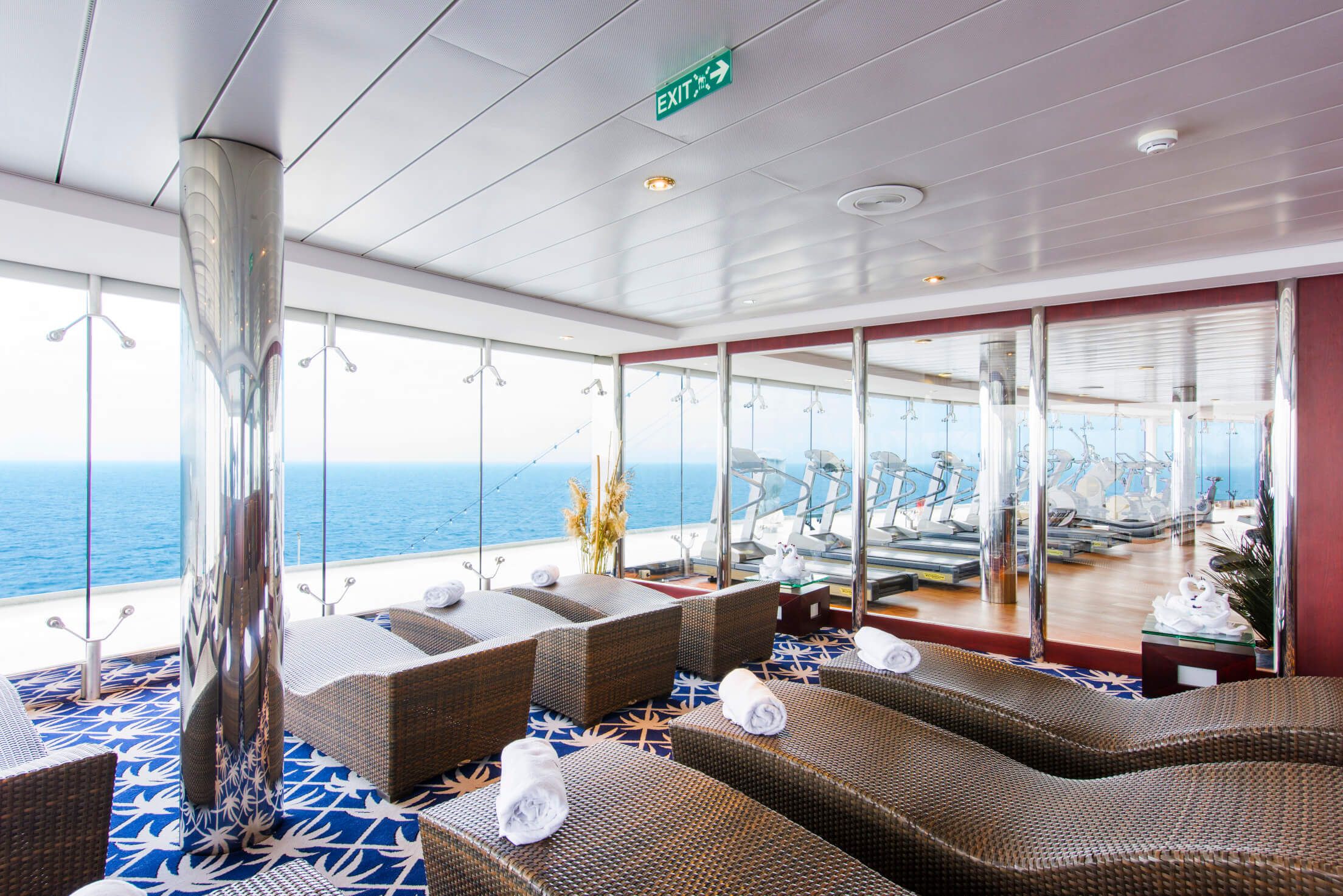 Ein schöner Wellnessbereich auf einem Schiff mit Ausblick auf das Meer und modernen Fitnessgeräten.