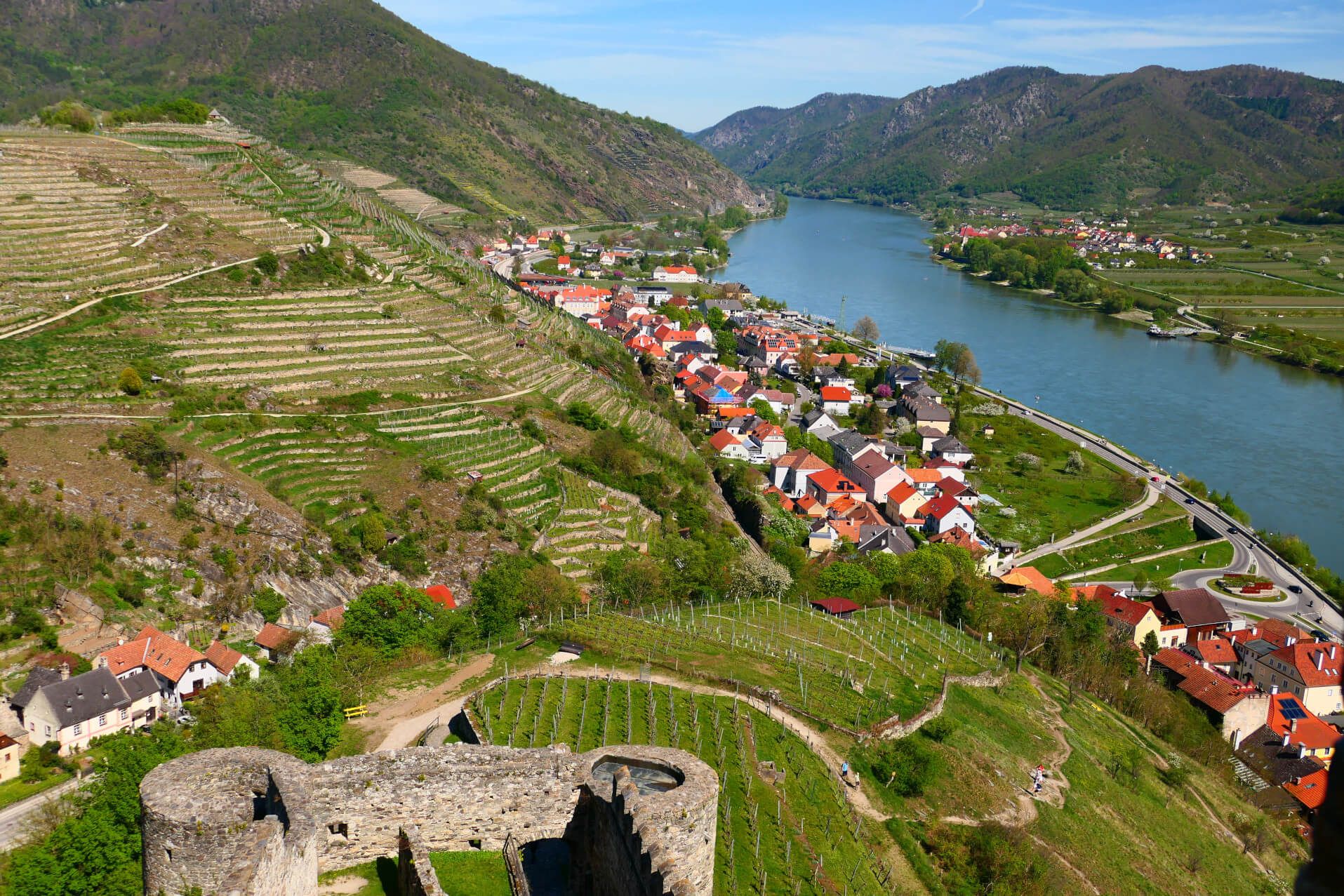 Eine malerische Landschaft mit Weinbergen, einem Fluss und bunten Häusern in den Hügeln.