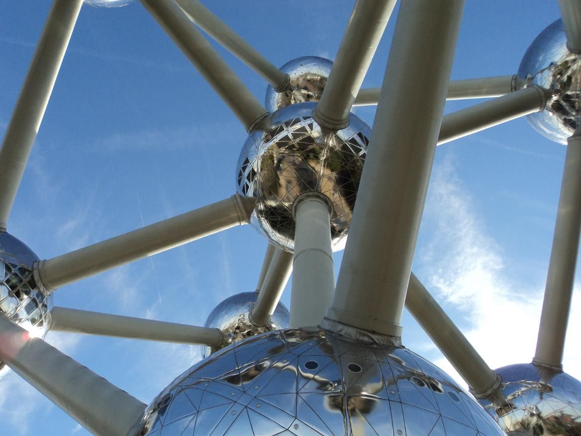 Das Bild zeigt die Struktur des Atomiums, mit seinen glänzenden Kugeln und Stützen vor einem blauen Himmel.
