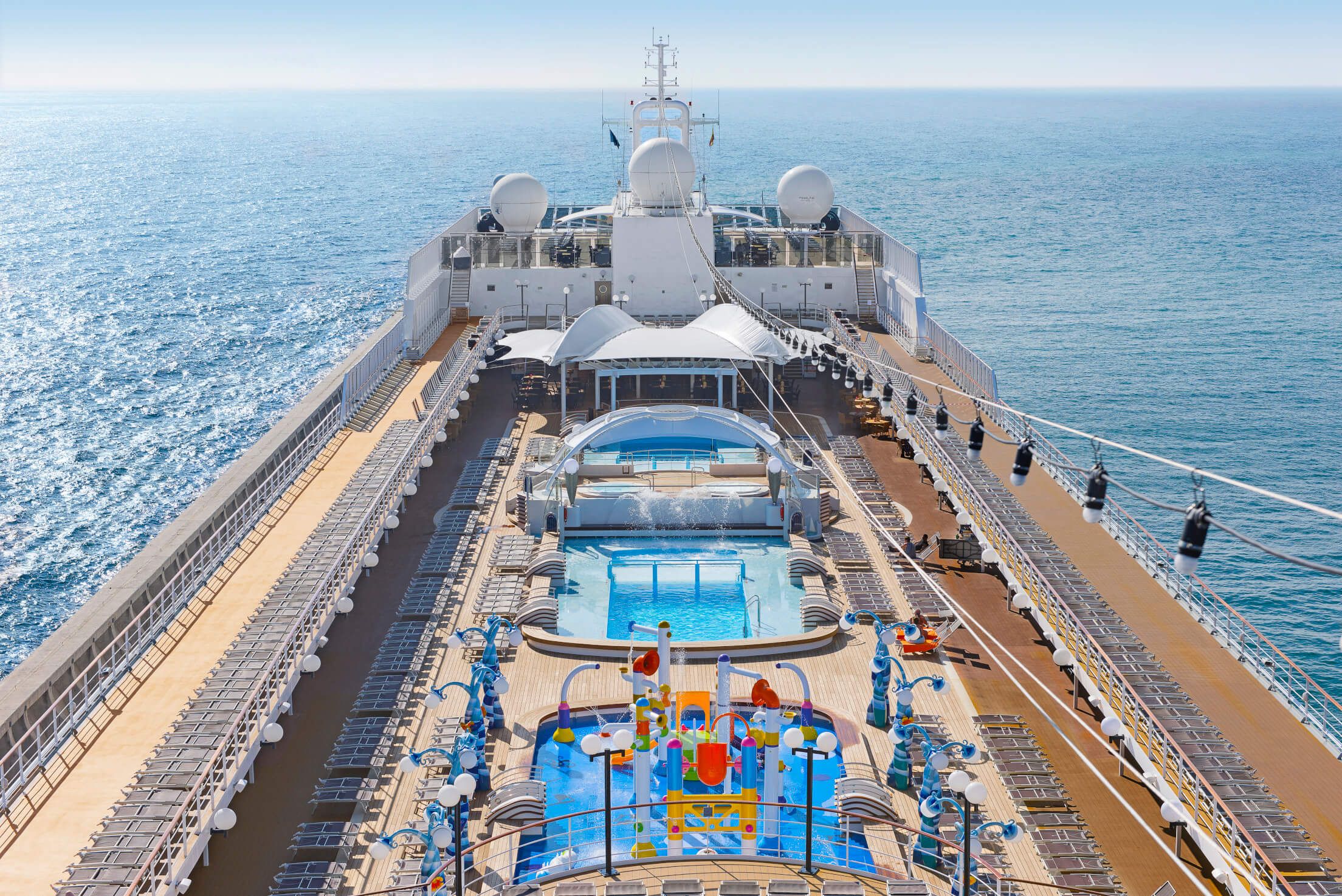 Ein großes Kreuzfahrtschiff mit Pool und Wasserpark auf dem Deck, umgeben von Meer und blauen Himmel.