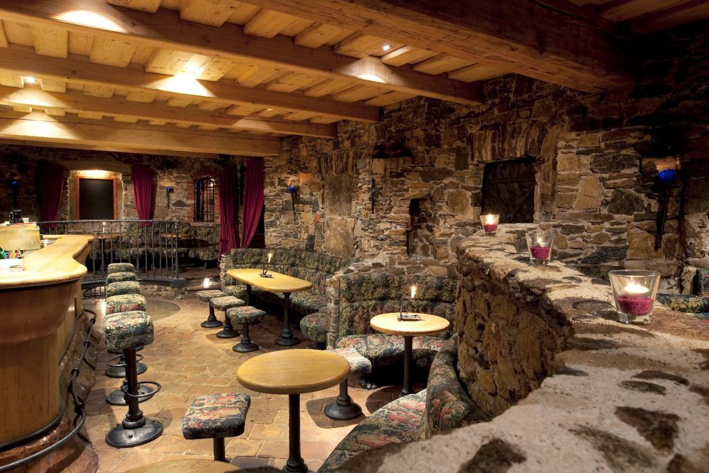 Gemütliche Bar mit steinernen Wänden, Holzdecke und Sitzgelegenheiten, romantisch beleuchtet von Kerzen.