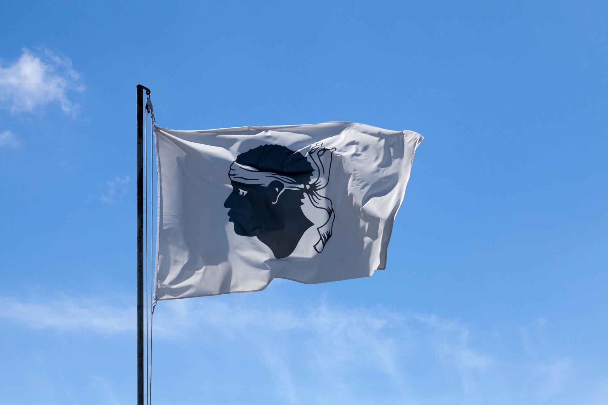 Eine weiße Flagge mit dem schwarzen Profil eines Mannes und blauen Himmel im Hintergrund.