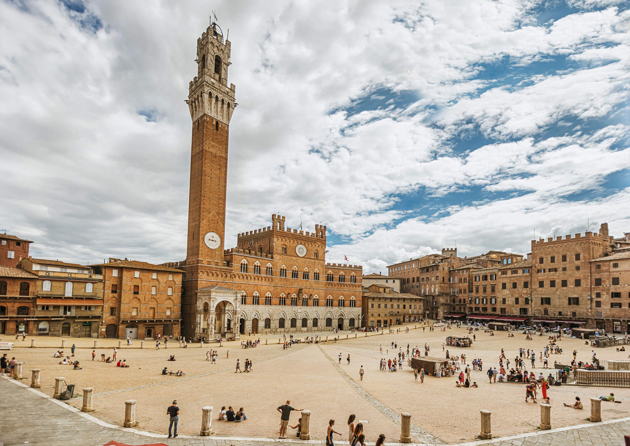 Piazza del Campo in Siena, umgeben von historischen Gebäuden, Menschen genießen die Atmosphäre unter bewölktem Himmel.