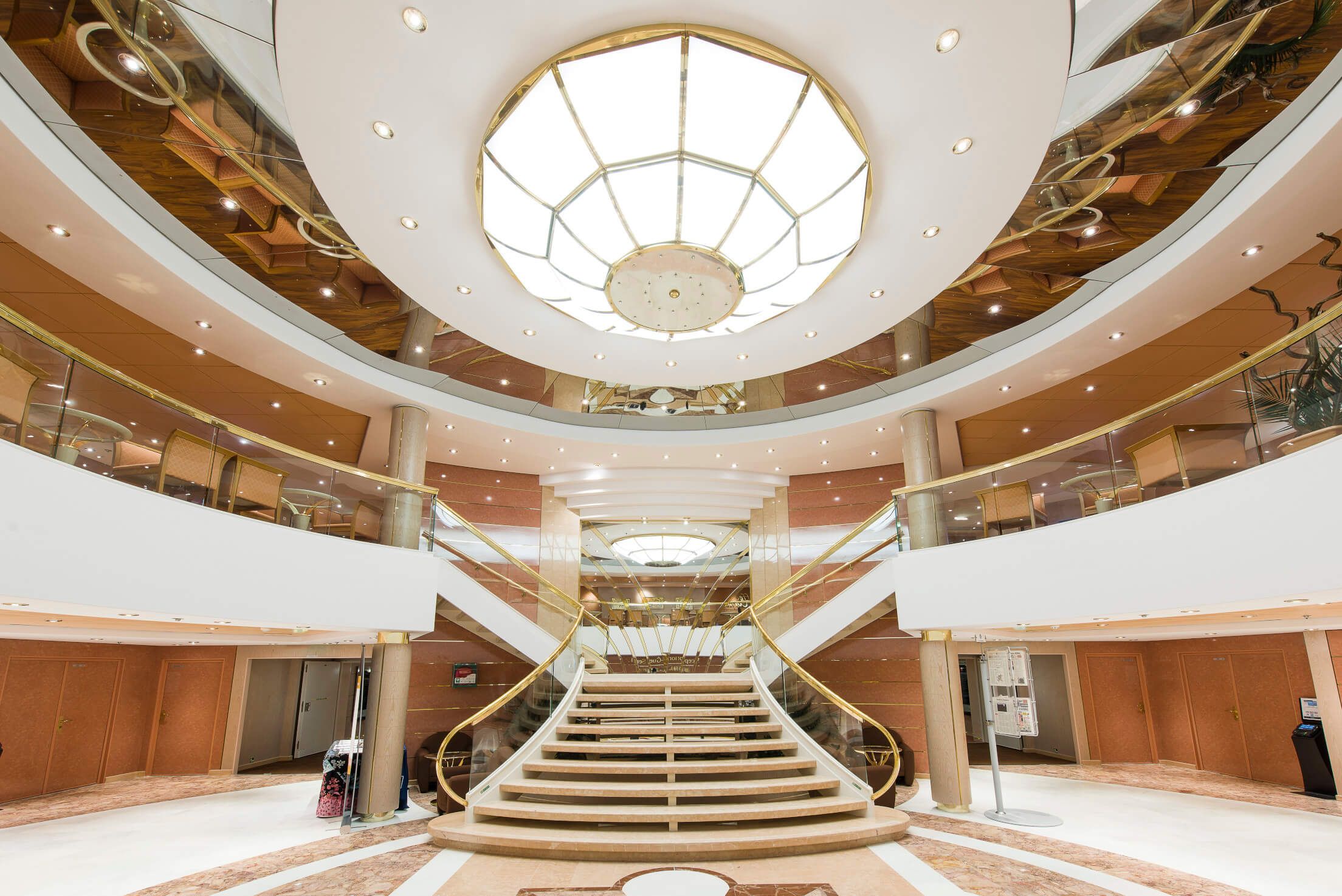 Elegante Treppe in einer stilvollen Halle mit runder Deckenbeleuchtung und gläsernen Geländern.