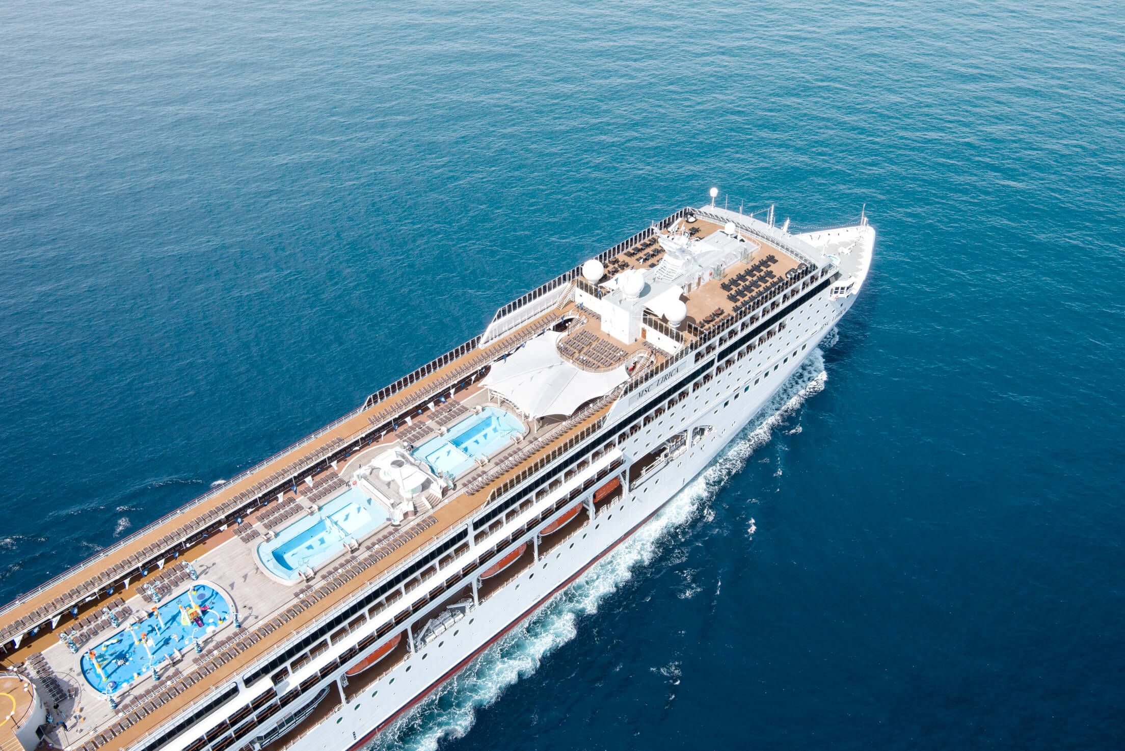 Ein Kreuzfahrtschiff schwebt über dem tiefblauen Wasser, mit Pools und Liegen auf dem Oberdeck.