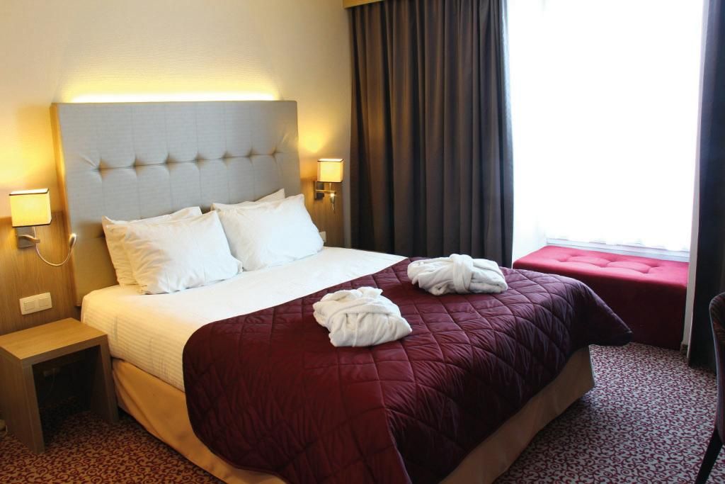 Ein modernes Zimmer mit einem großen Bett, eleganter Bettwäsche und einer gemütlichen Sitzecke am Fenster.