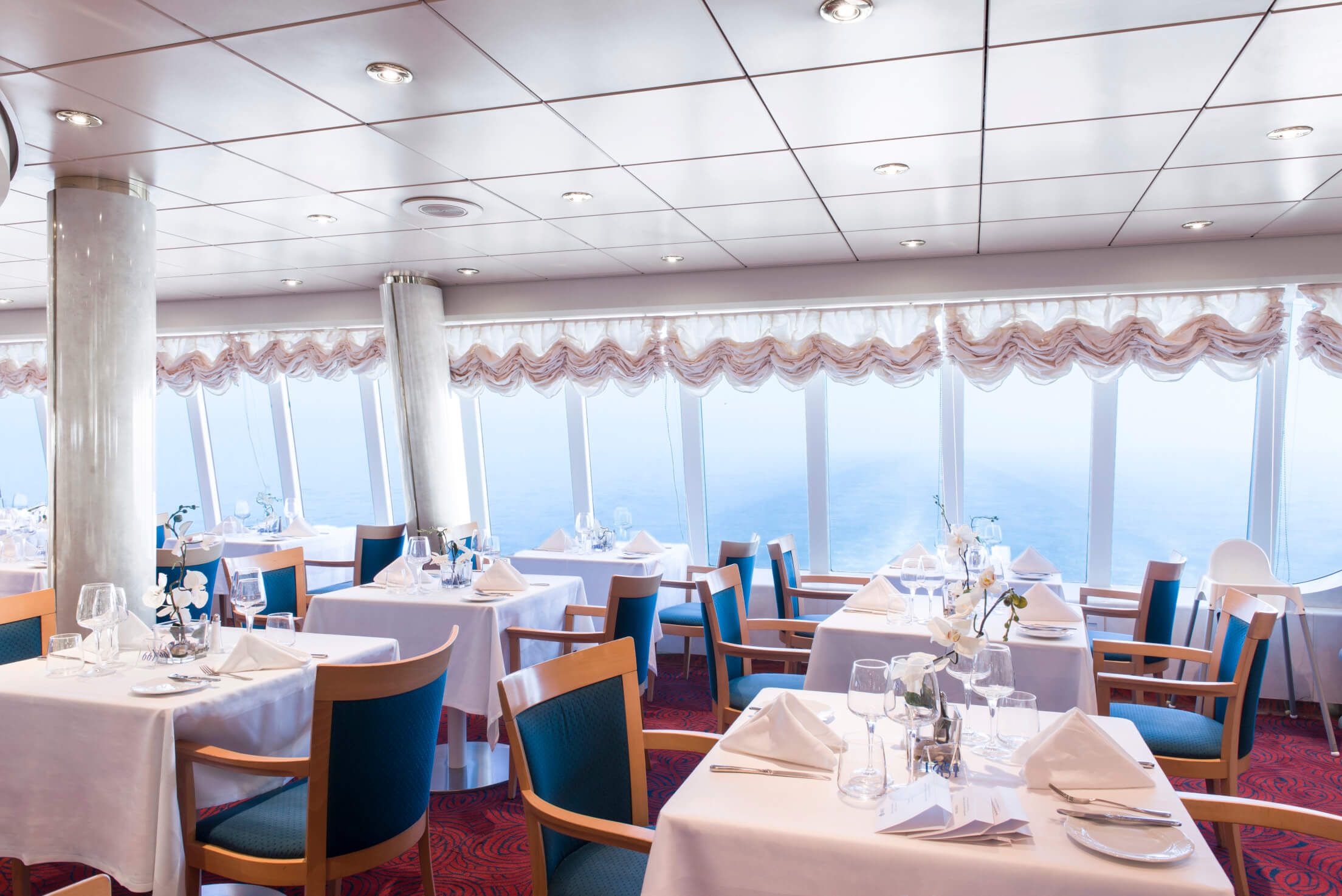 Elegantes Restaurant mit Meerblick, weißen Tischtüchern und modernen Möbeln, gemütliche Atmosphäre und Dekoration.