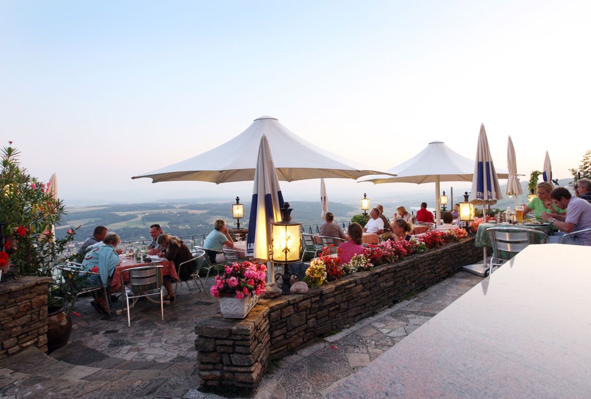 Eine Terrasse mit Gästen, Sonnenschirmen und Blumen, bietet einen schönen Blick auf die Umgebung bei Dämmerung.