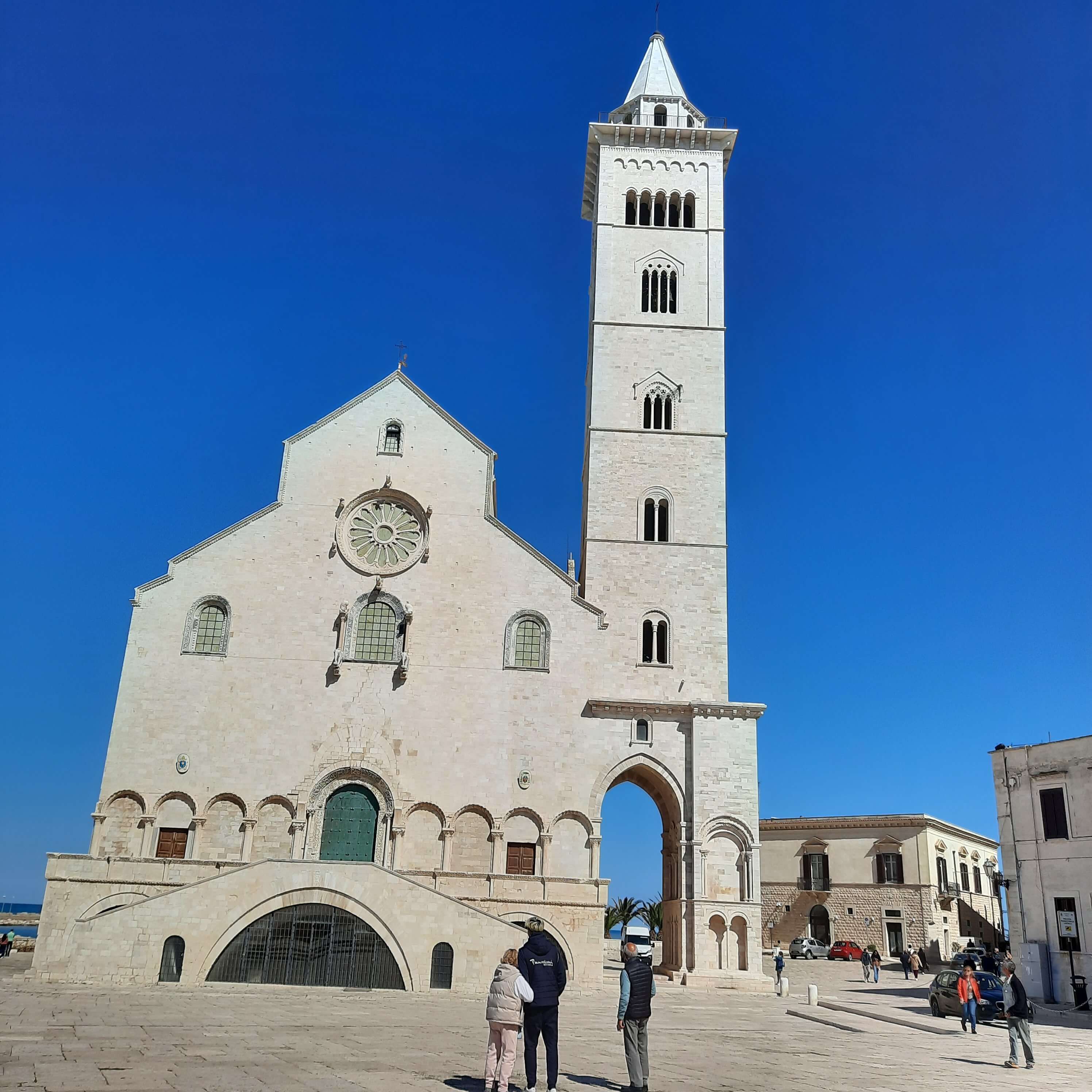 Eine beeindruckende Kirche mit einem hohen Glockenturm und blauem Himmel, Menschen erkunden den Platz.