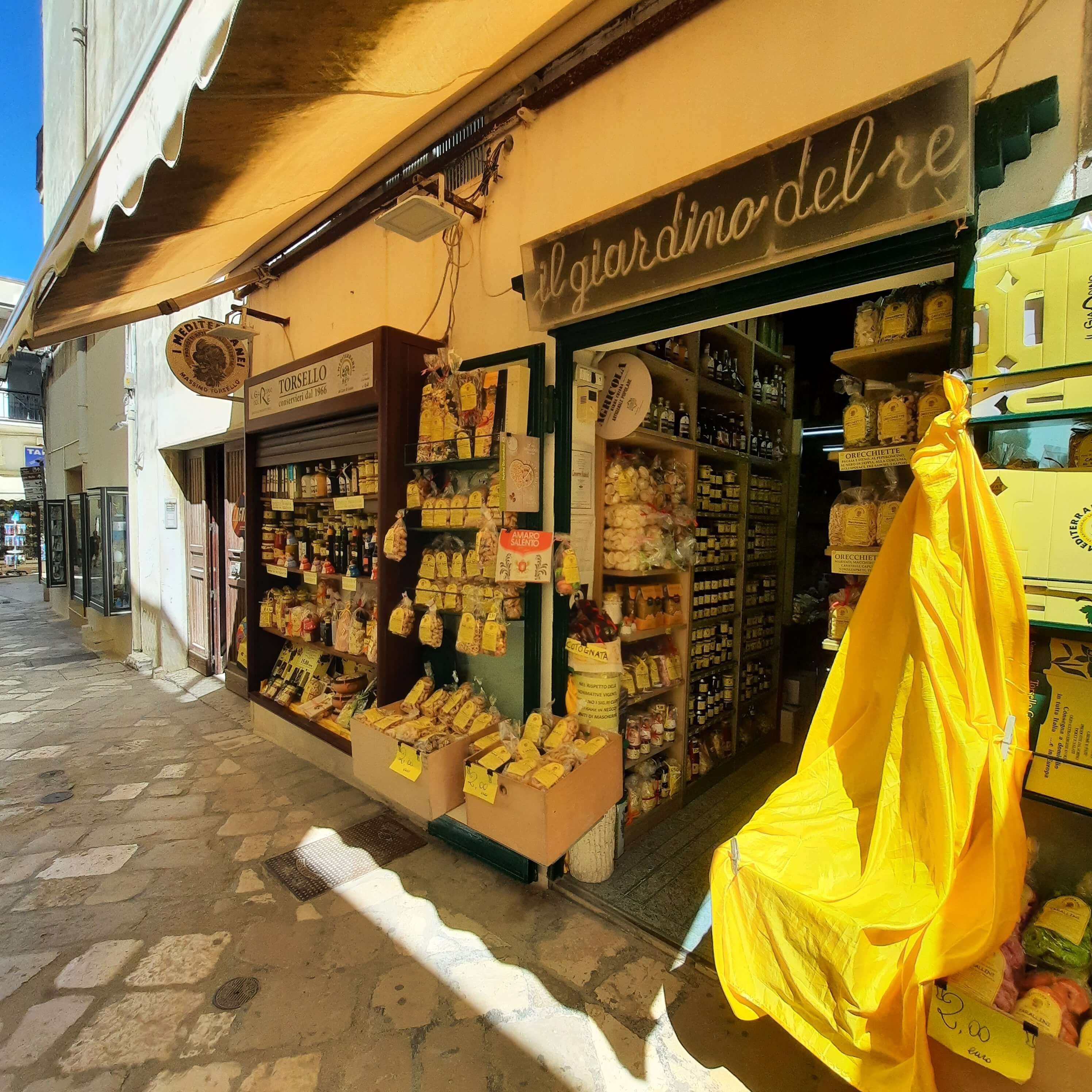 Ein einladender Laden mit bunten Produkten, darunter viele Lebensmittel, in einer charmanten Gasse.