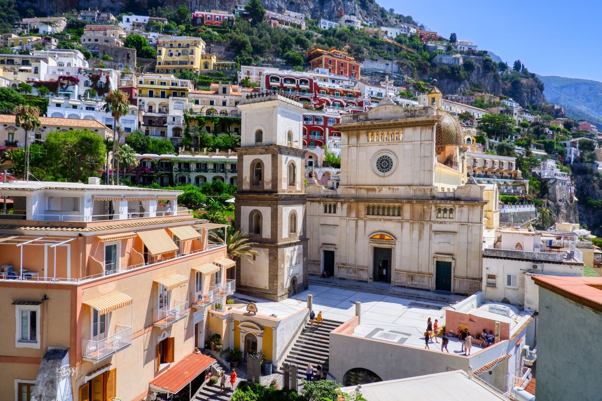 Positano, Italien: Bunte Häuser am Hang, die Kirche mit der markanten Kuppel und lebhafte Menschen auf der Piazza.