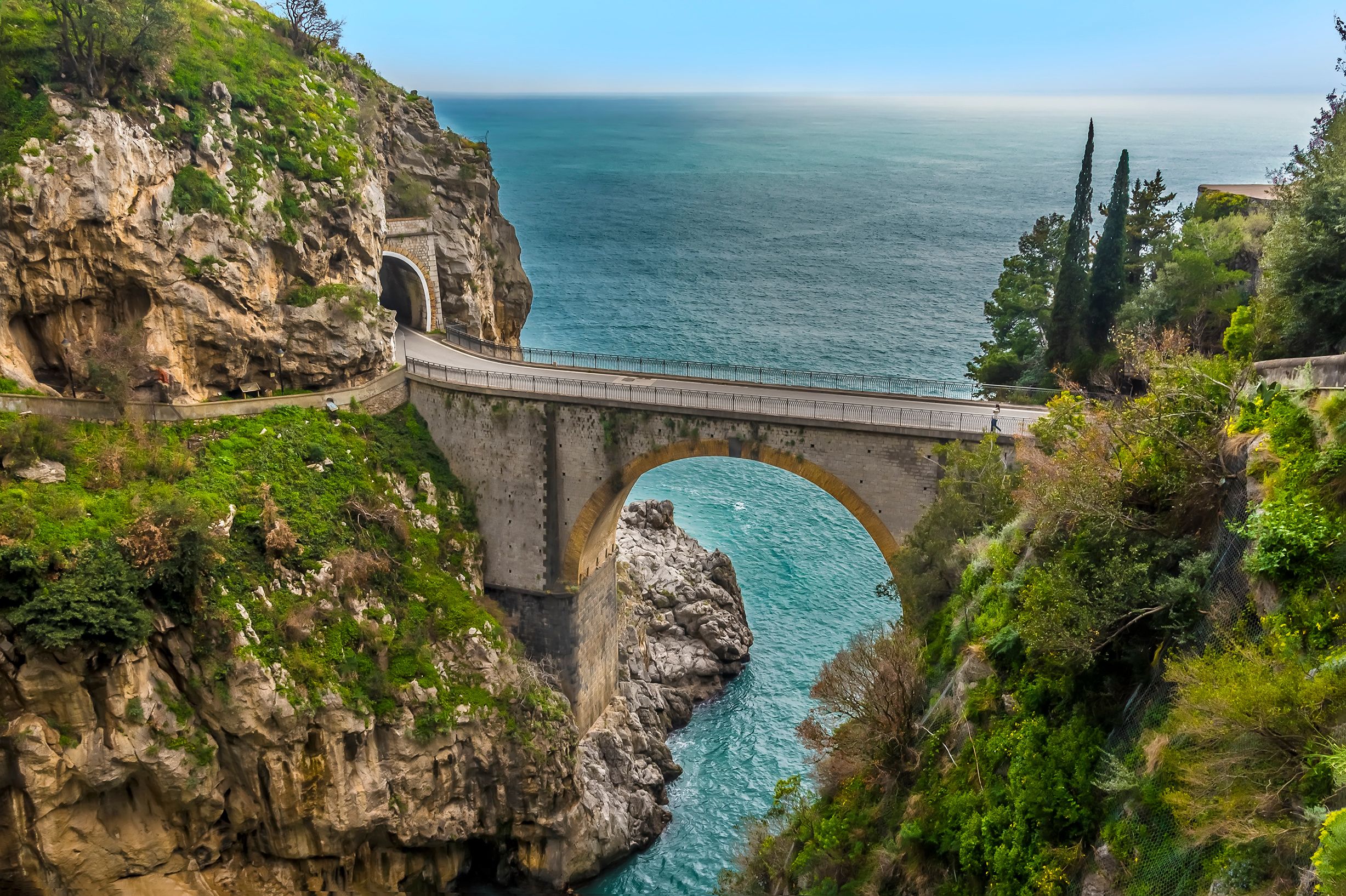 Eine malerische Brücke über dem türkisfarbenen Wasser, umgeben von steilen Klippen und üppigem Grün.