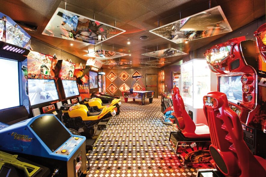 Ein buntes Spielzimmer mit klassischen Arcade-Automaten, Rennspielen und einem Tisch für Unterhaltung.