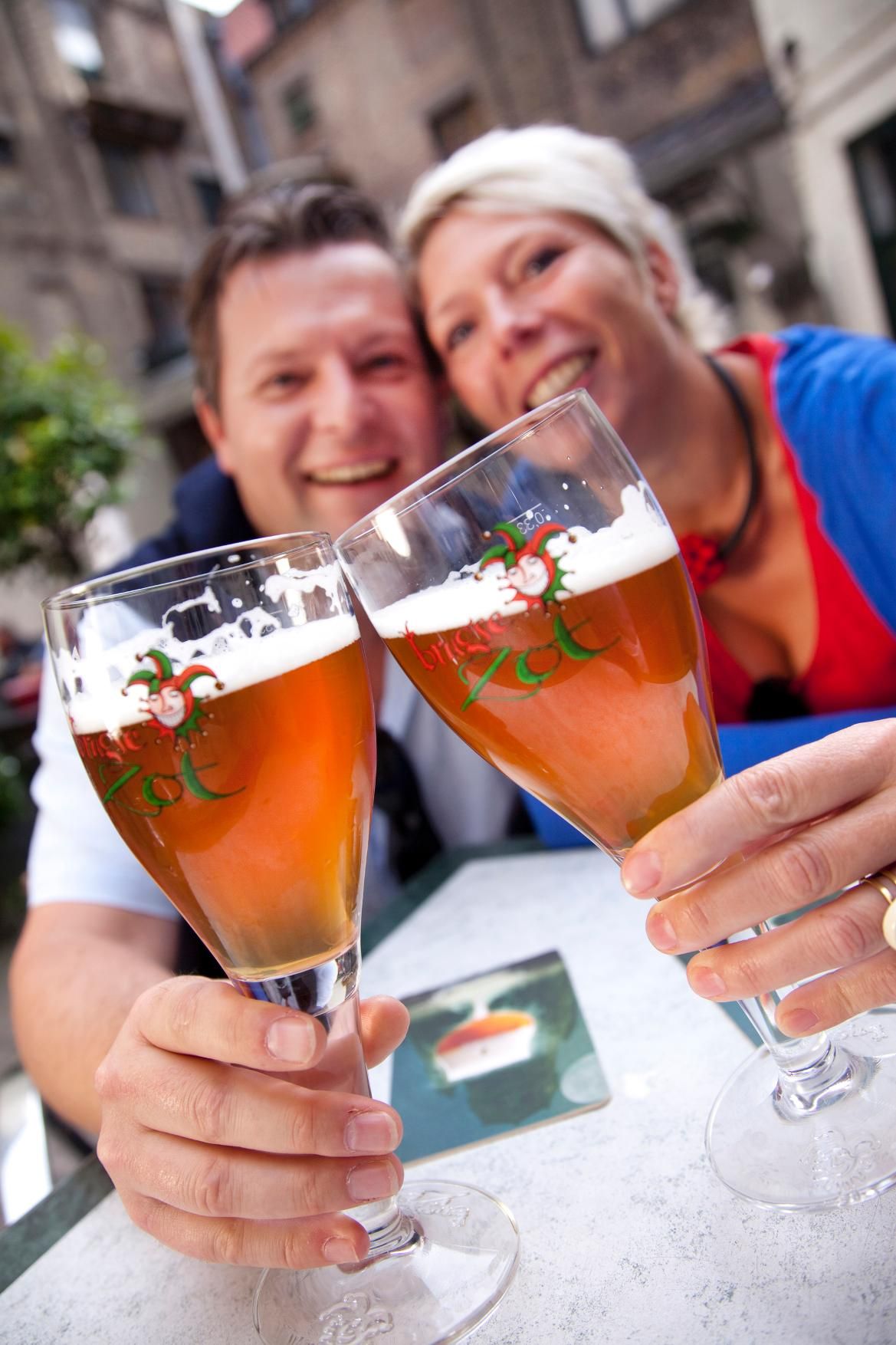 Zwei fröhliche Personen stoßen mit Biergläsern an, umgeben von einer gemütlichen Umgebung.