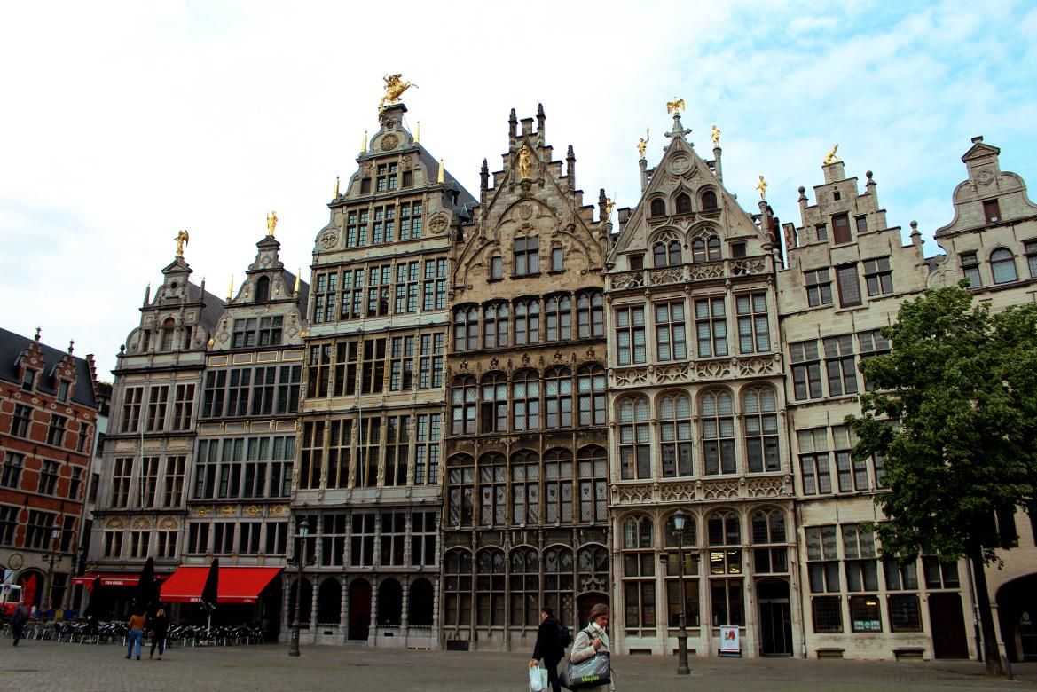 Historische Gebäude mit prächtigen Fassaden in Antwerpen, darunter goldene Statuen und ein klarer Himmel.
