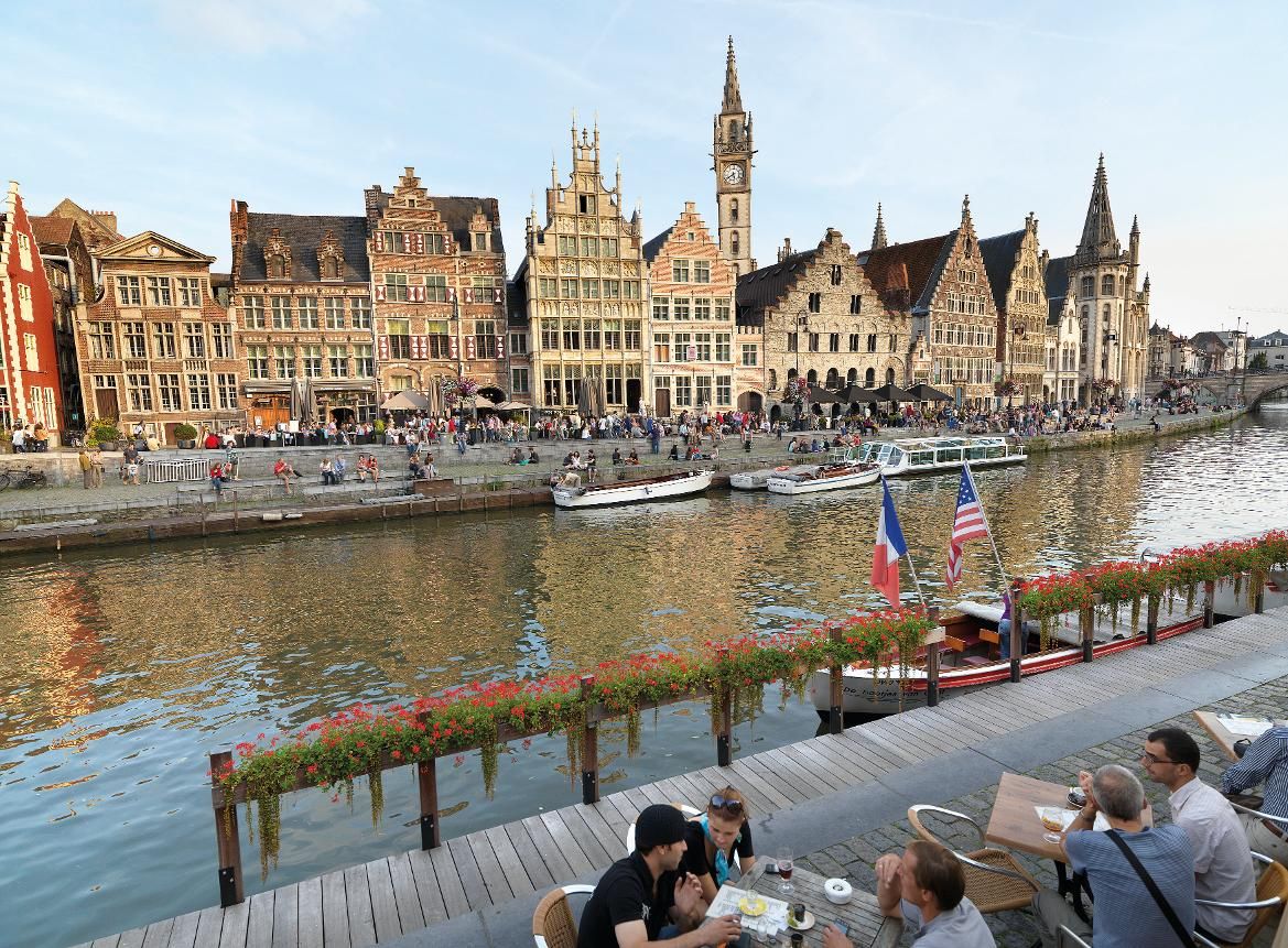 Eine malerische Uferpromenade mit historischen Gebäuden, Booten und Menschen, die das Leben am Wasser genießen.
