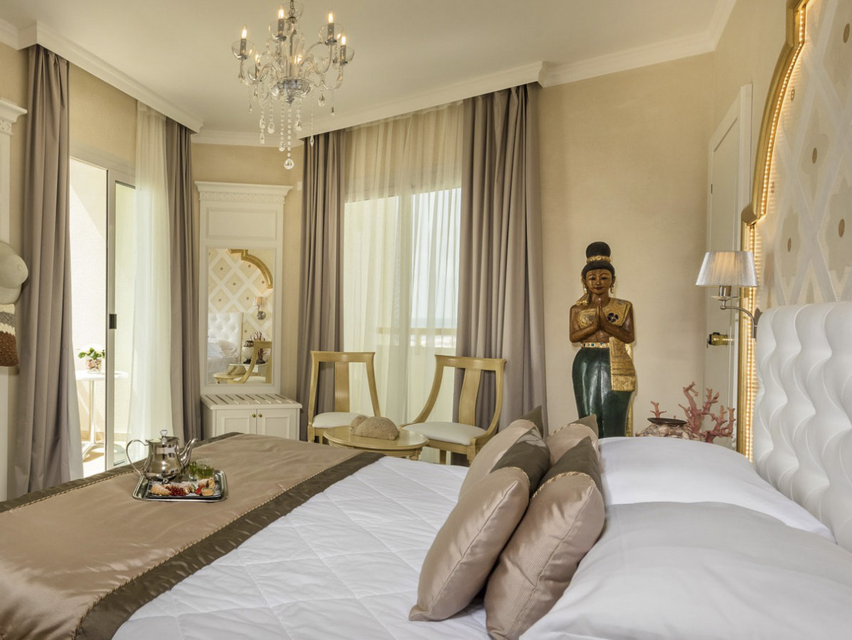 Elegantes Schlafzimmer mit Kristallleuchte, Sitzbereich, Spiegel und einer Statue in traditionellem Stil.