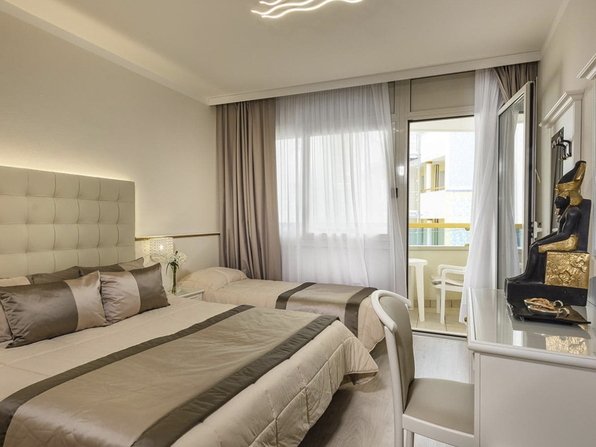 Ein modernes Schlafzimmer mit einem Doppelbett, Einzelbett, Schreibtisch und einem Balkonzugang. Helle, elegante Farben.