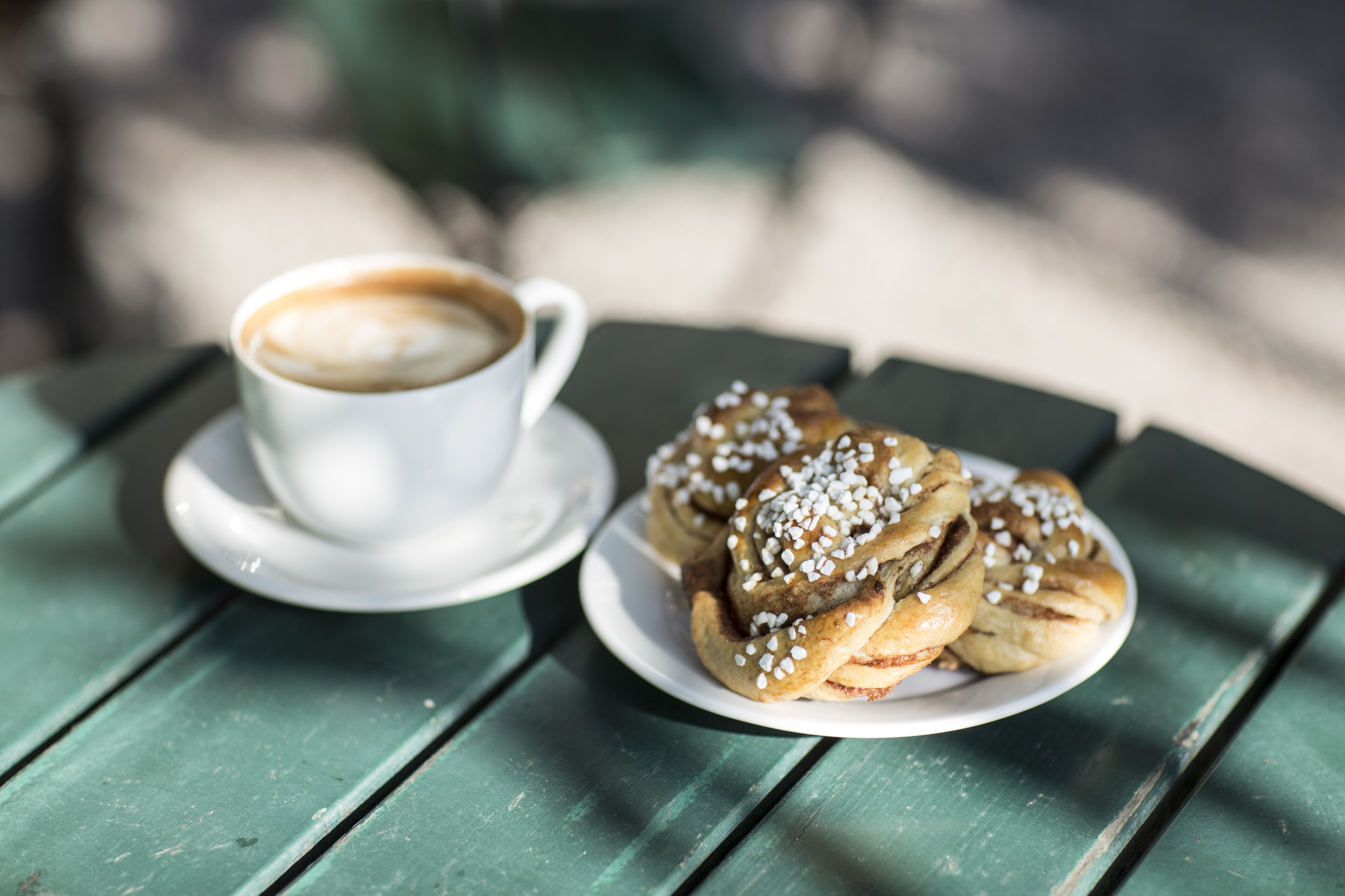 Eine Tasse Kaffee steht neben einem Teller mit Zimtschnecken, dekoriert mit Zuckerstreuseln.