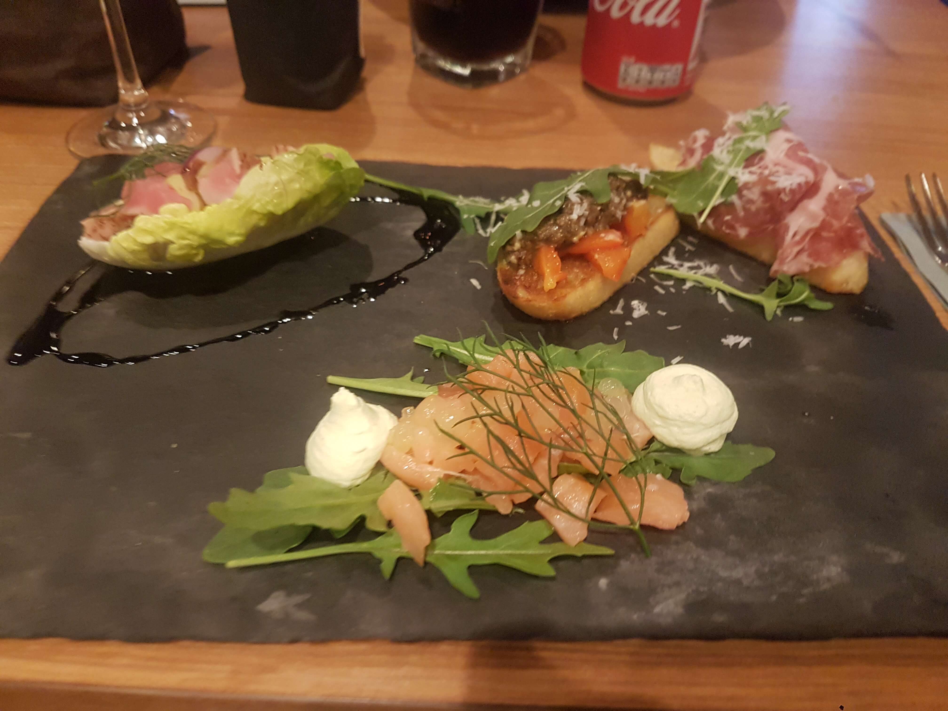 Ein stilvolles Gericht auf einem schwarzen Stein: Salat, Räucherlachs und Bruschetta mit verschiedenen Belägen.