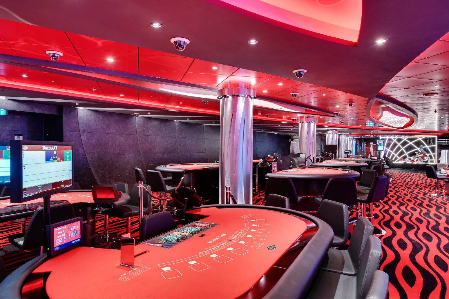 Elegantes Casino mit roten Tönen, Tischspielen und moderner Ausstattung in stilvollem Ambiente.