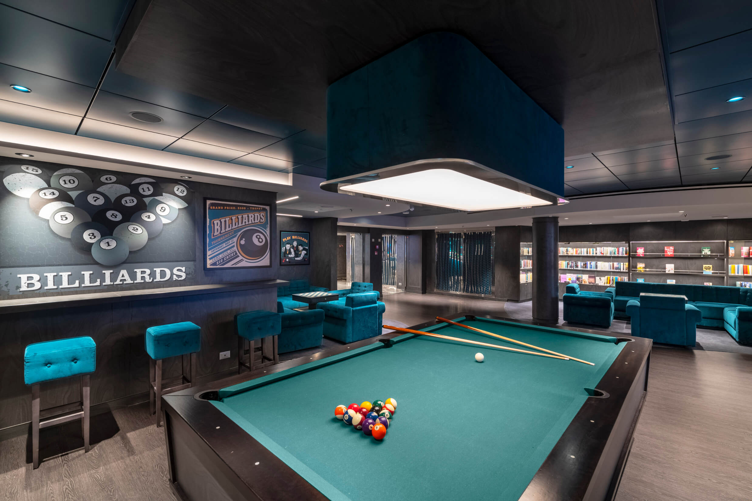 Ein moderner Billardraum mit einem Tisch, bunten Kugeln und gemütlichen blauen Sitzmöbeln im Hintergrund.