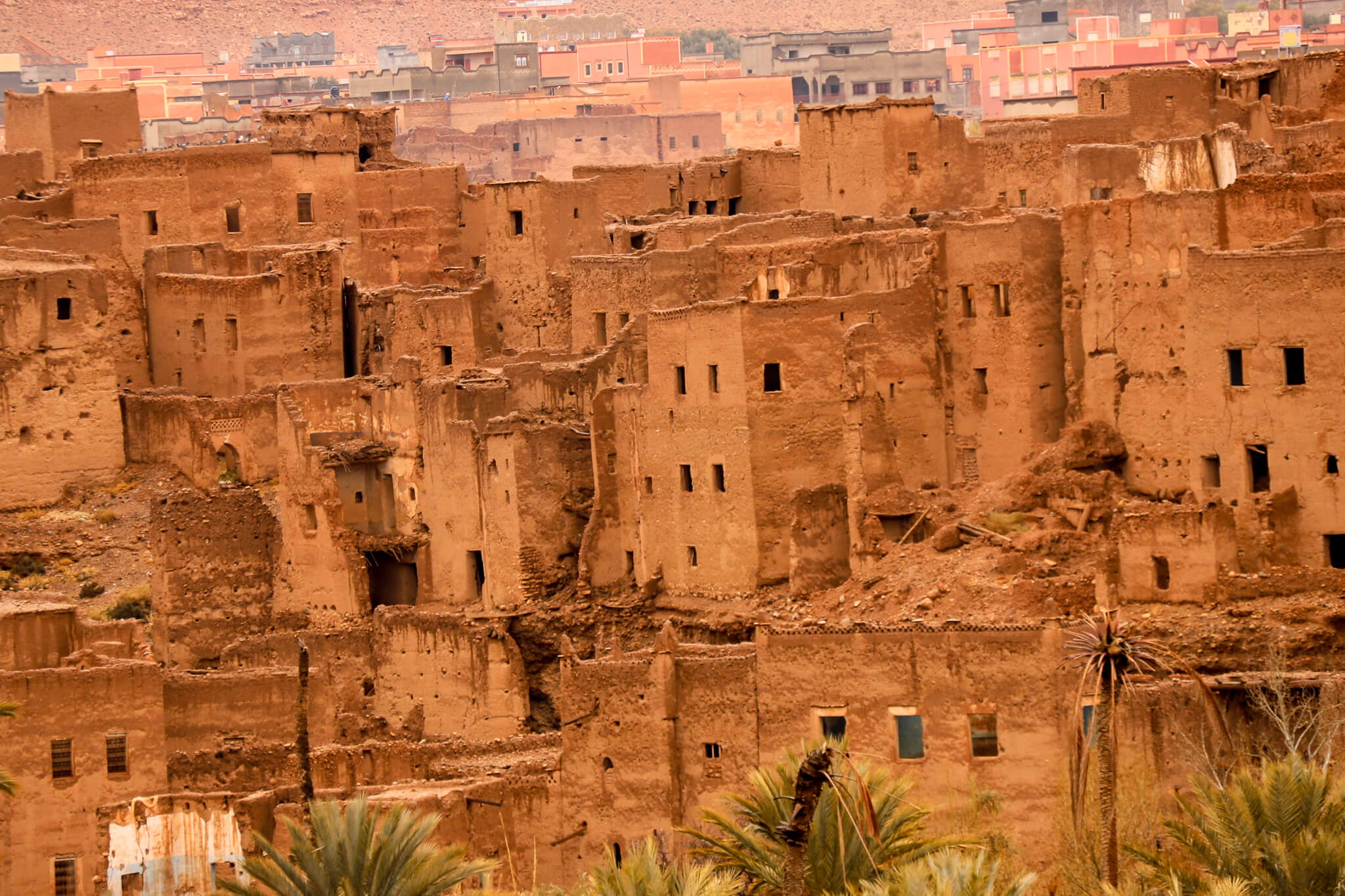 Eine alte Lehmbau-Siedlung, die von der Zeit gezeichnet ist, umgeben von Wüste und Palmen.