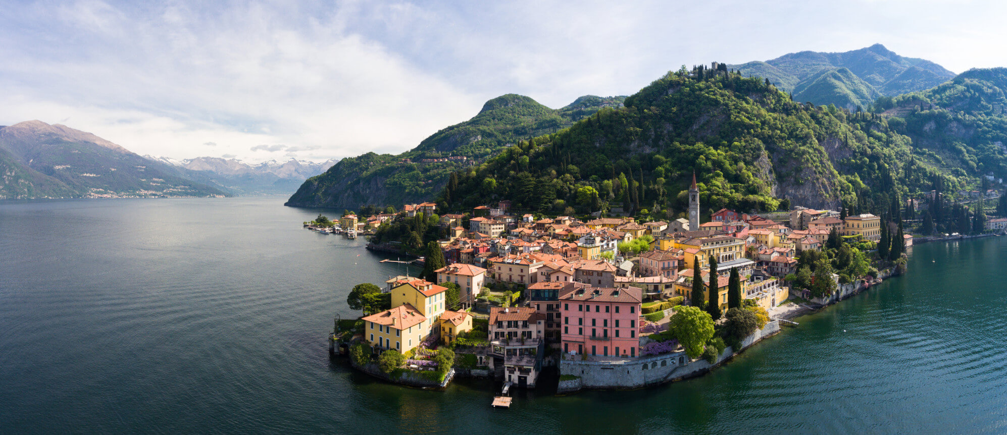 Ein malerisches Dorf am Ufer eines ruhigen Sees, umgeben von üppigen Bergen und klaren Himmel.