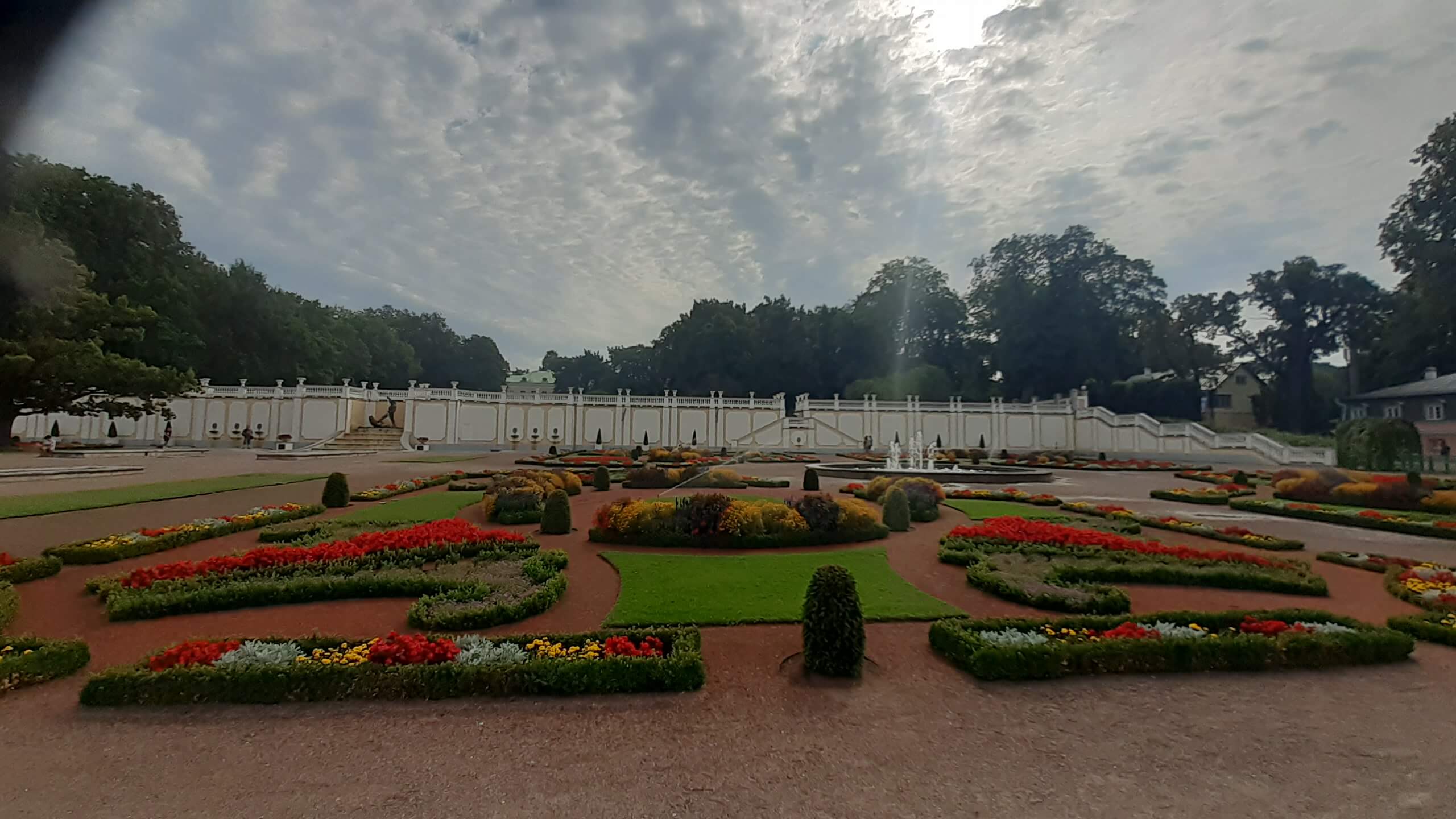 Ein schöner Garten mit bunten Blumenbeeten, umgeben von einer weißen Mauer und Bäumen im Hintergrund.
