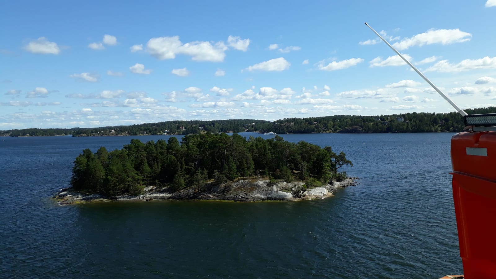 Eine kleine grüne Insel im azurblauen Wasser unter wolkigem Himmel. Frische, natürliche Landschaft.