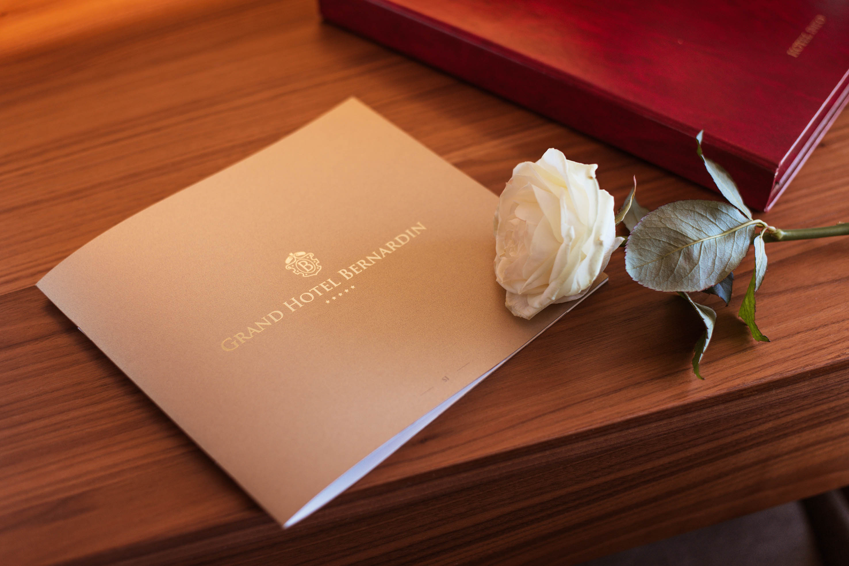 Eine elegante Broschüre des Grand Hotel Bernardin mit einer weißen Rose auf einem Holztisch.