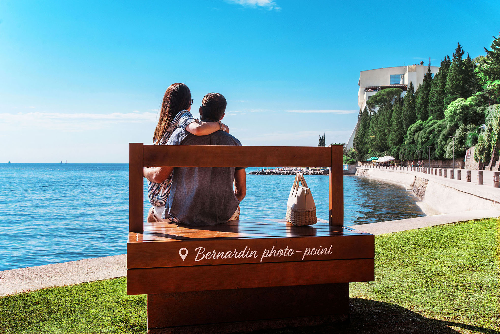 Ein Paar sitzt auf einer Bank am Wasser, genießt den Ausblick und die Sonne an einem schönen Tag.