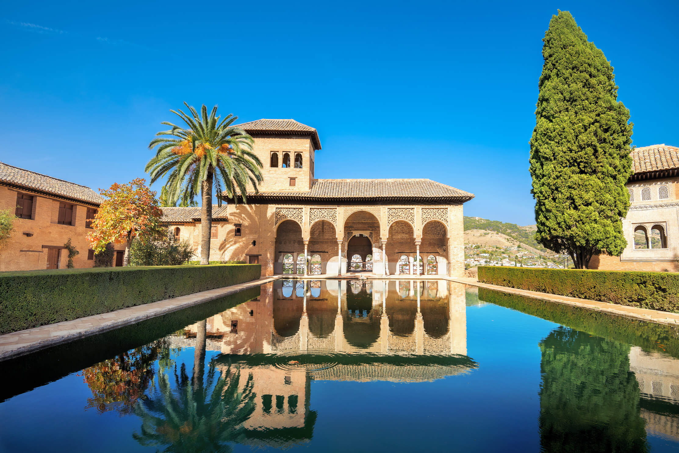 Die Alcazaba von Granada spiegelt sich im ruhigen Wasser eines kanarischen Gartens unter klarem blauen Himmel.