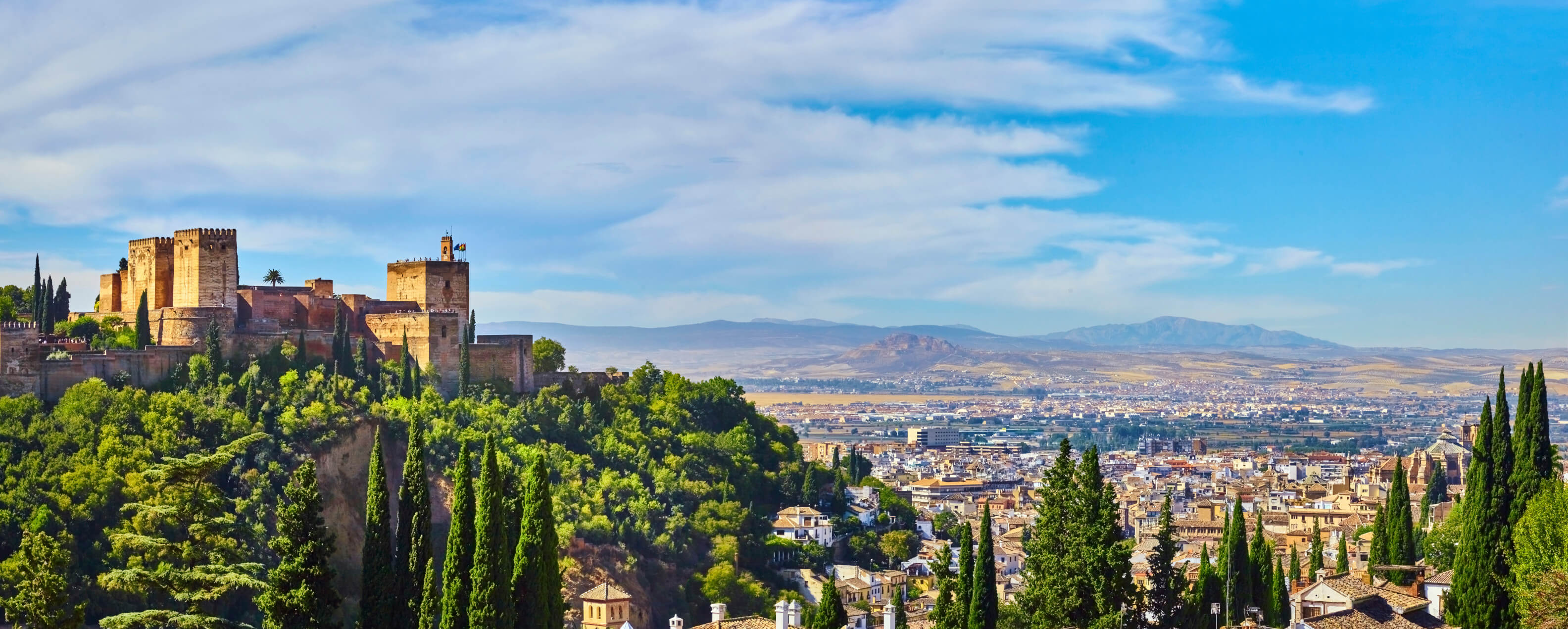 Die Alhambra thronet über Granada, umgeben von üppigem Grün und weitem Blick auf die Stadt und Berge.