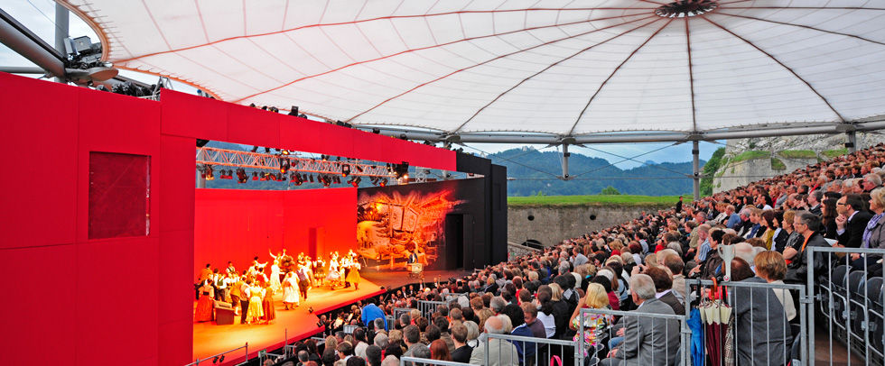 Eine faszinierende Bühne mit einem vollen Publikum, das eine Live-Aufführung unter einem großen Zeltdach genießt.