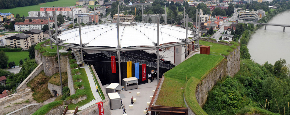 Eine Luftaufnahme einer modernen Veranstaltungsstätte auf einer alten Festung mit Blick auf die Stadt und den Fluss.