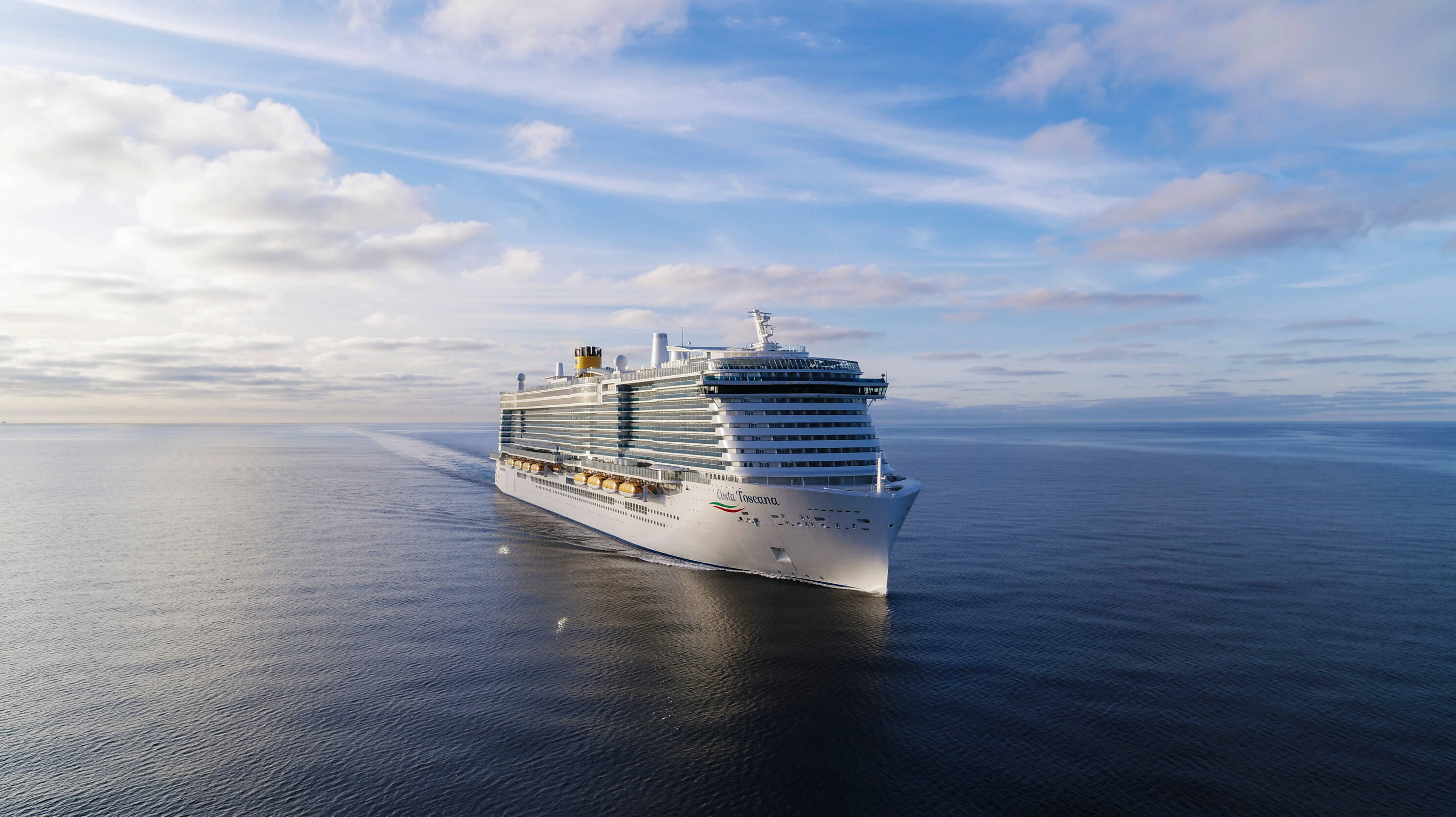 Ein großes Kreuzfahrtschiff fährt über ruhiges, weites Wasser unter einem bewölkten Himmel.