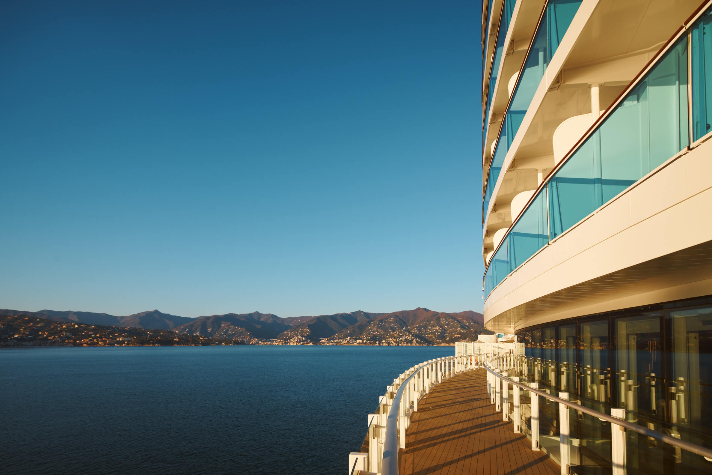 Ein schönes Meer mit Bergen im Hintergrund und einem modernen Schiff, dessen Deck sanft im Sonnenlicht glänzt.