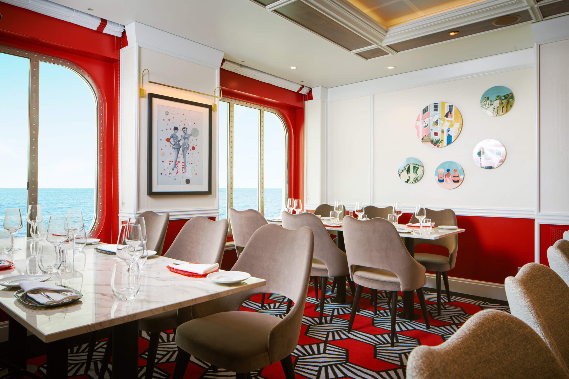 Ein elegantes Restaurant mit rotem Dekor, Meerblick und modernen Kunstwerken an den Wänden.