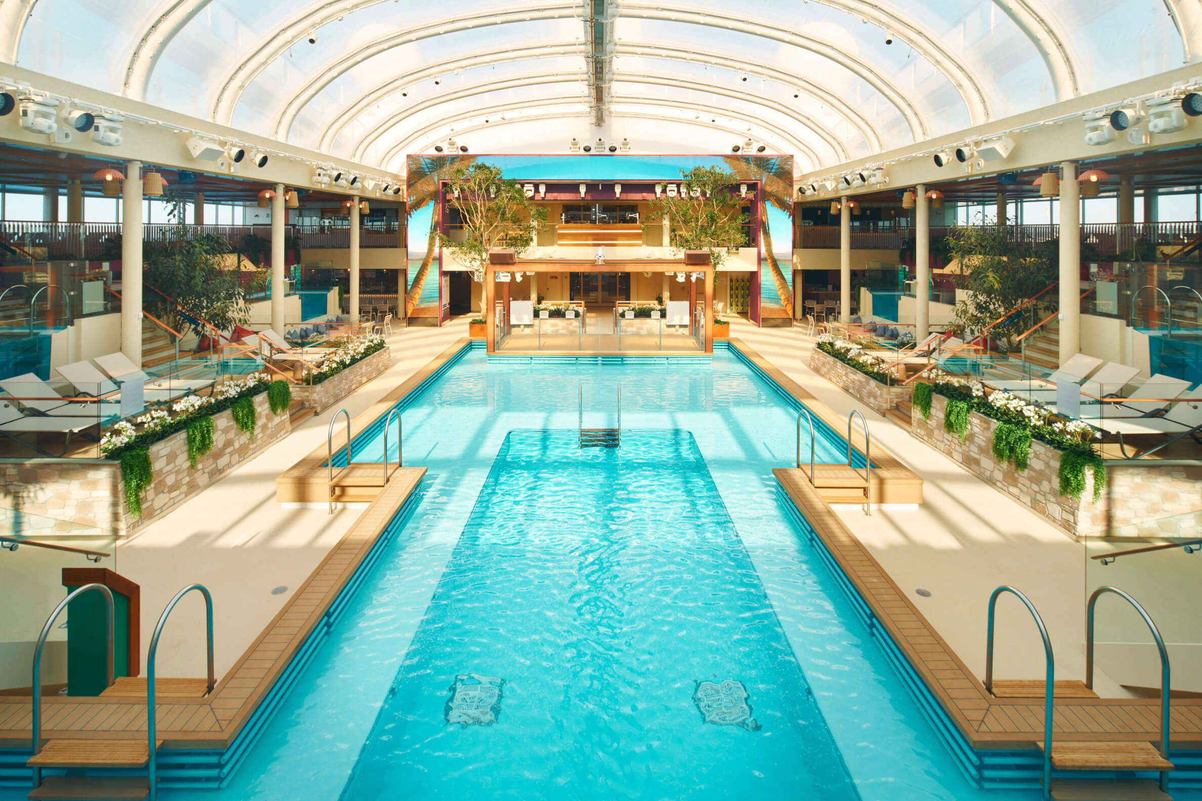 Ein modernes Hallenbad mit glasgedeckter Struktur, umgeben von Pflanzen und komfortablen Liegen.