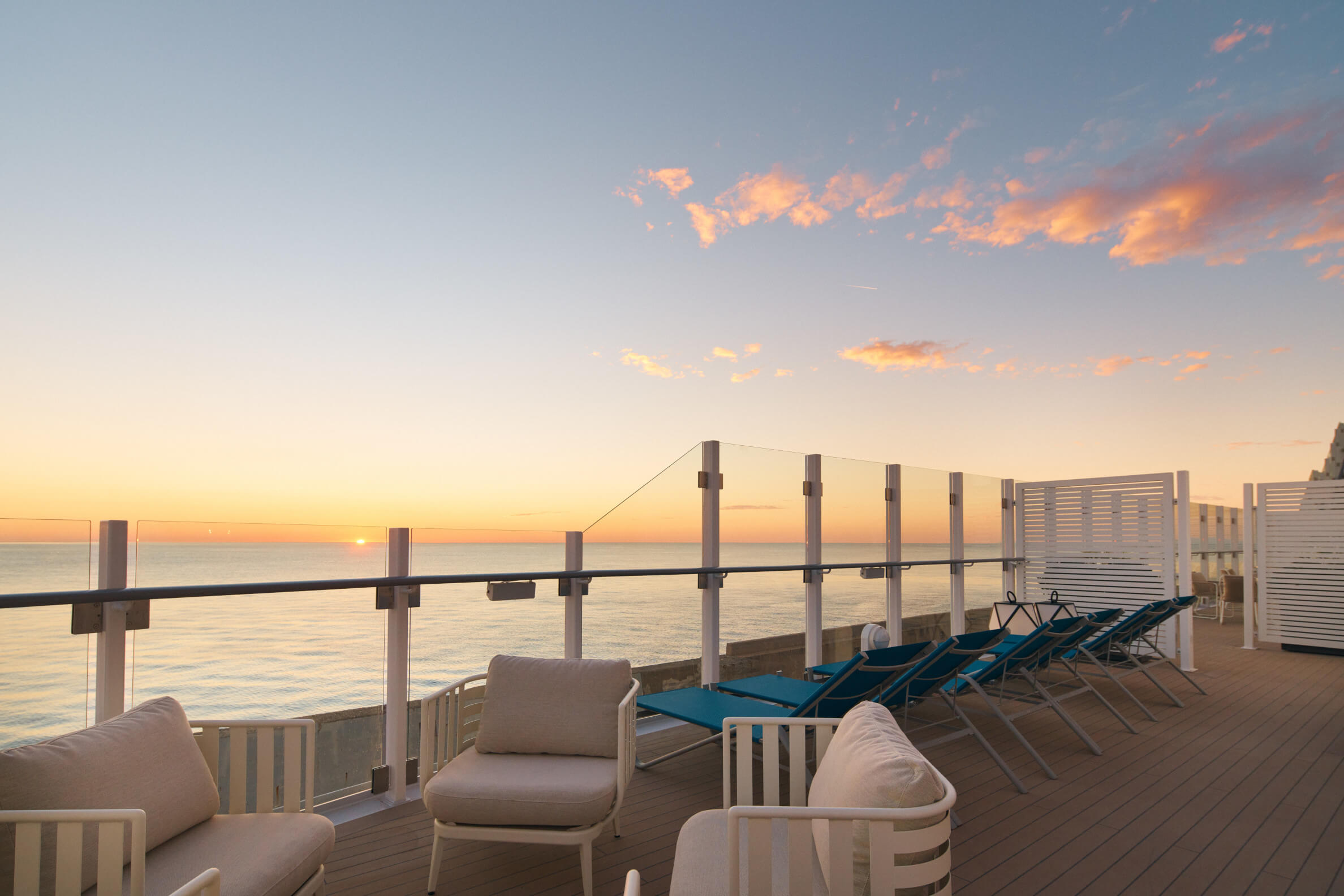 Terrasse mit loungemöbeln und Liegen, Blick auf den Sonnenuntergang über dem Meer in sanften Farben.