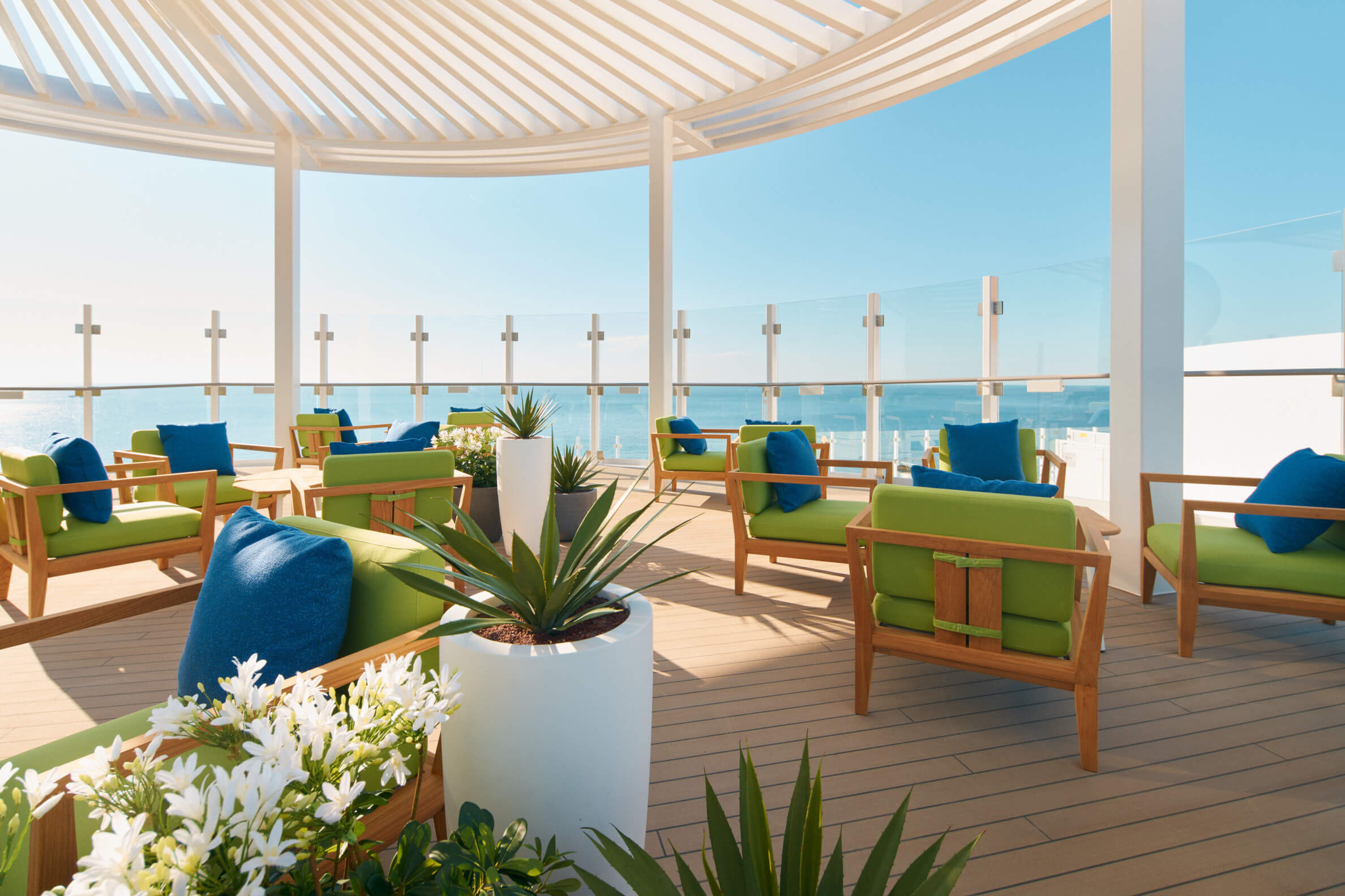Moderne Terrasse mit Blick auf das Meer, bequeme Sitze in Grün und Blau sowie Pflanzen umgeben die Lounge.